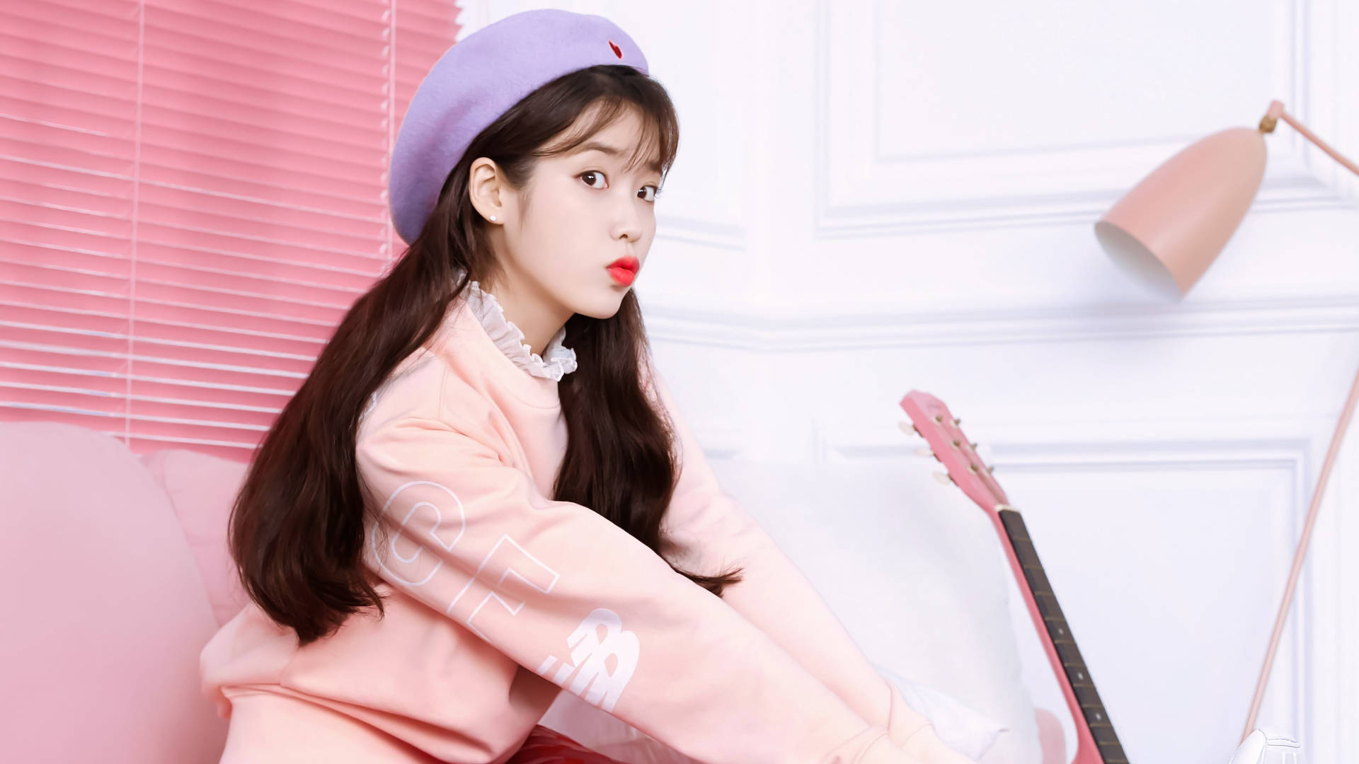 IU 身穿柔粉外套、紫色帽子，坐在柔粉沙發上，旁邊放著粉紅吉他。