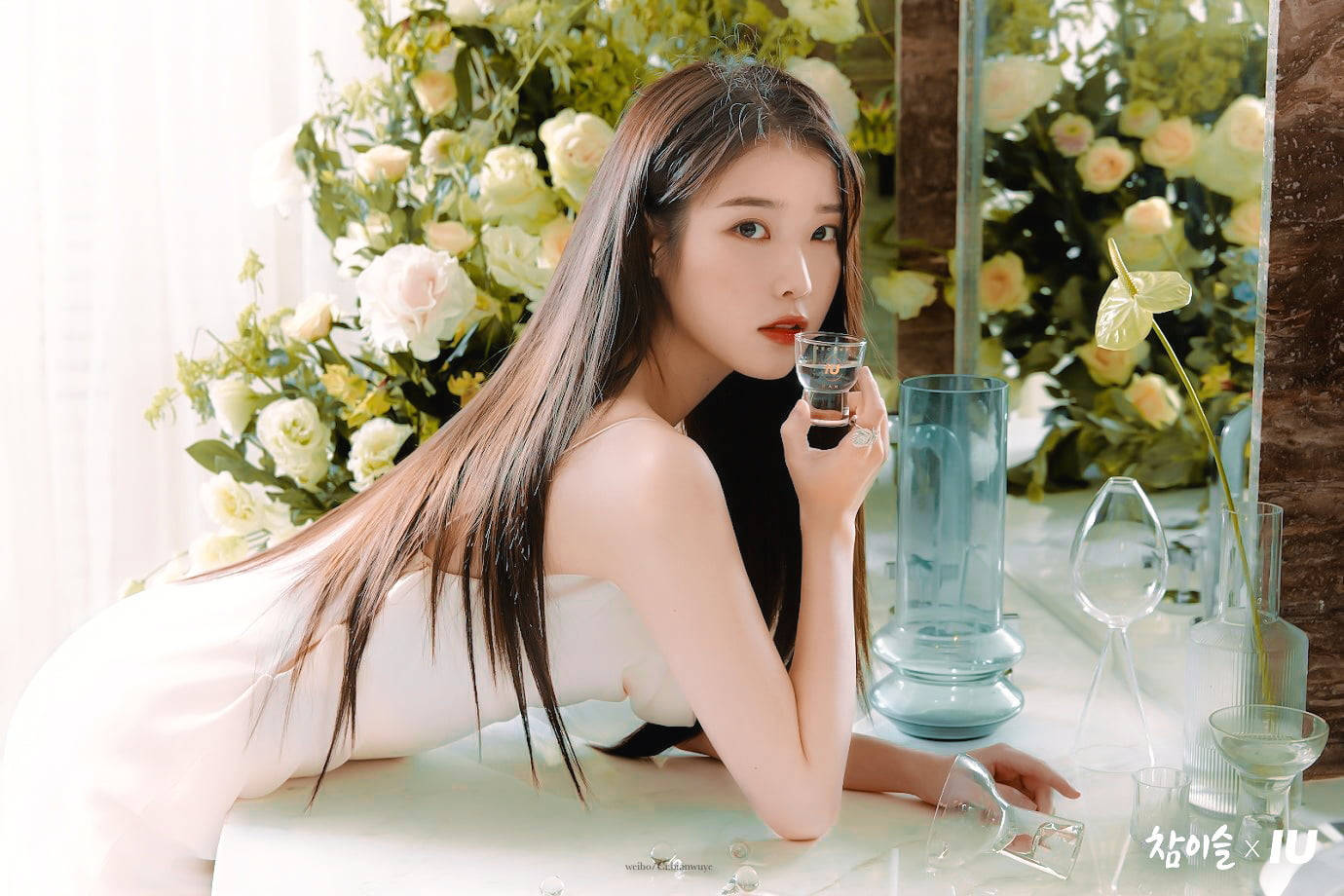 身穿白色連衣裙的女性手持酒杯，周圍環繞著花卉和玻璃器皿。