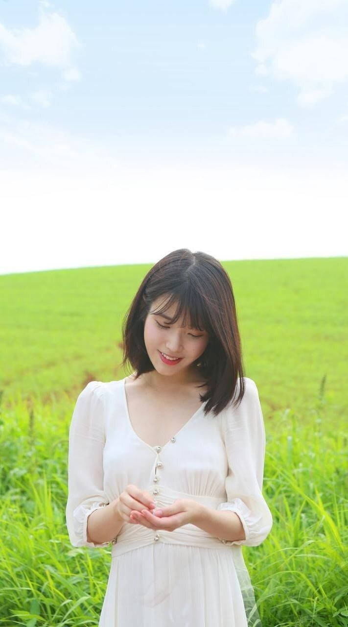 年輕女性穿白裙在草地微笑於晴天
