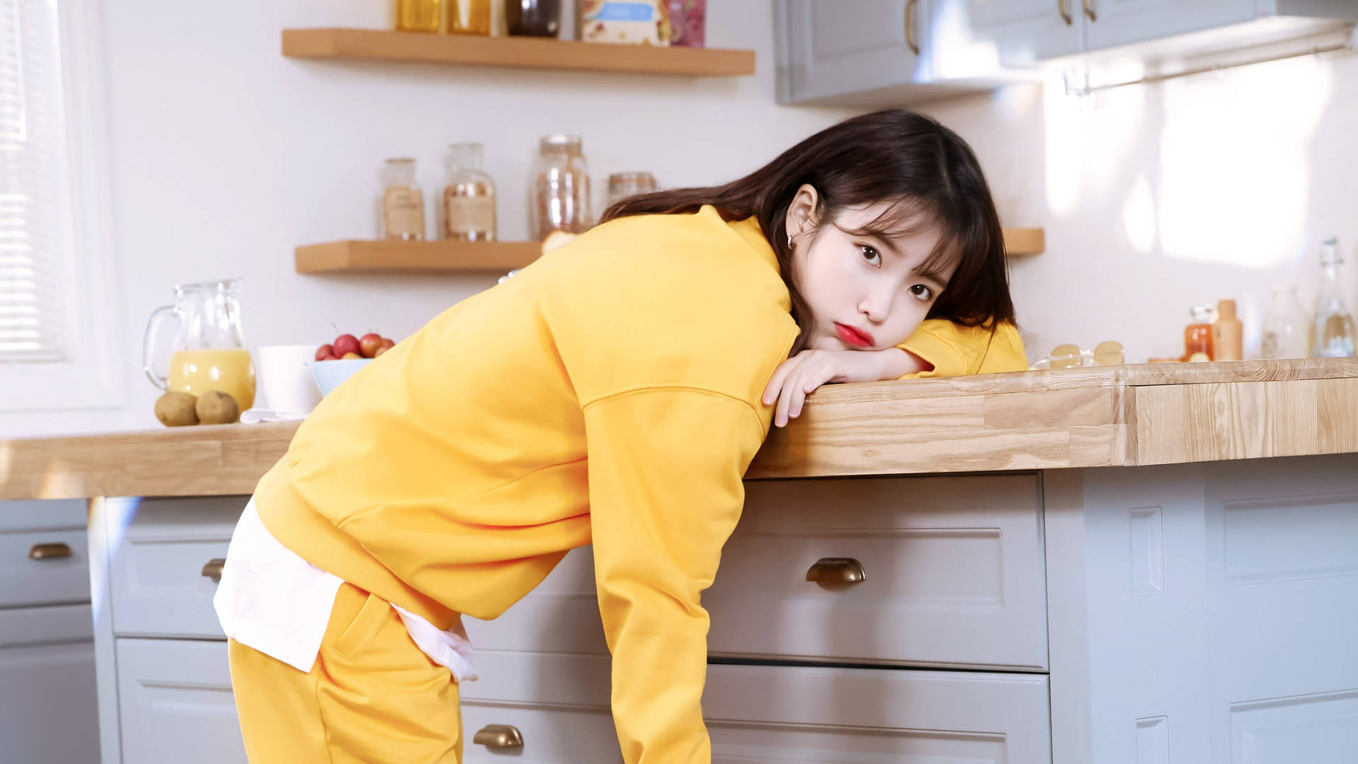 穿著黃色運動服的年輕女子靠在廚房檯面上，表情俏皮。