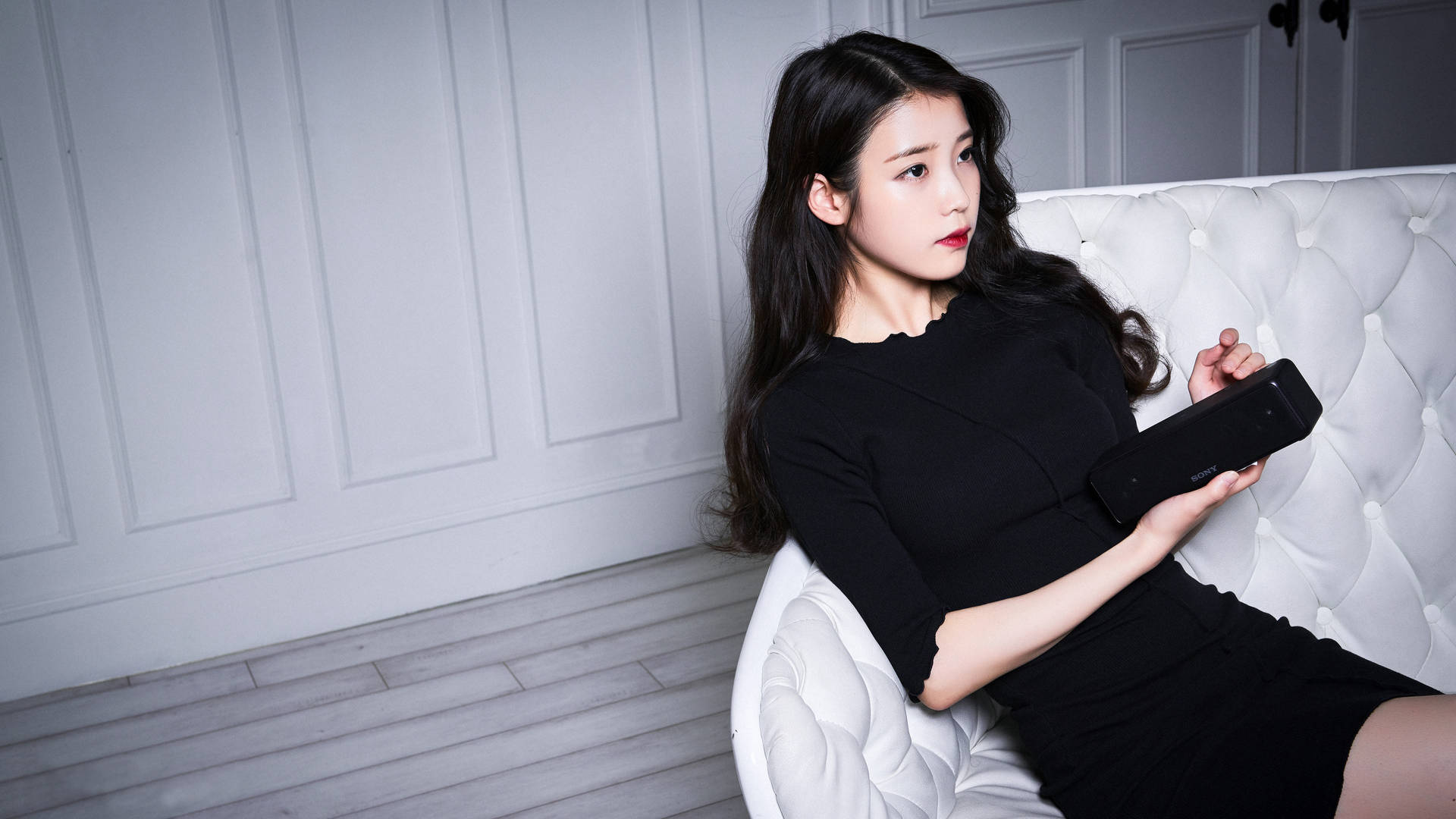 身穿黑色連衣裙的女性在現代房間的白色簇絨沙發上手持平板電腦。