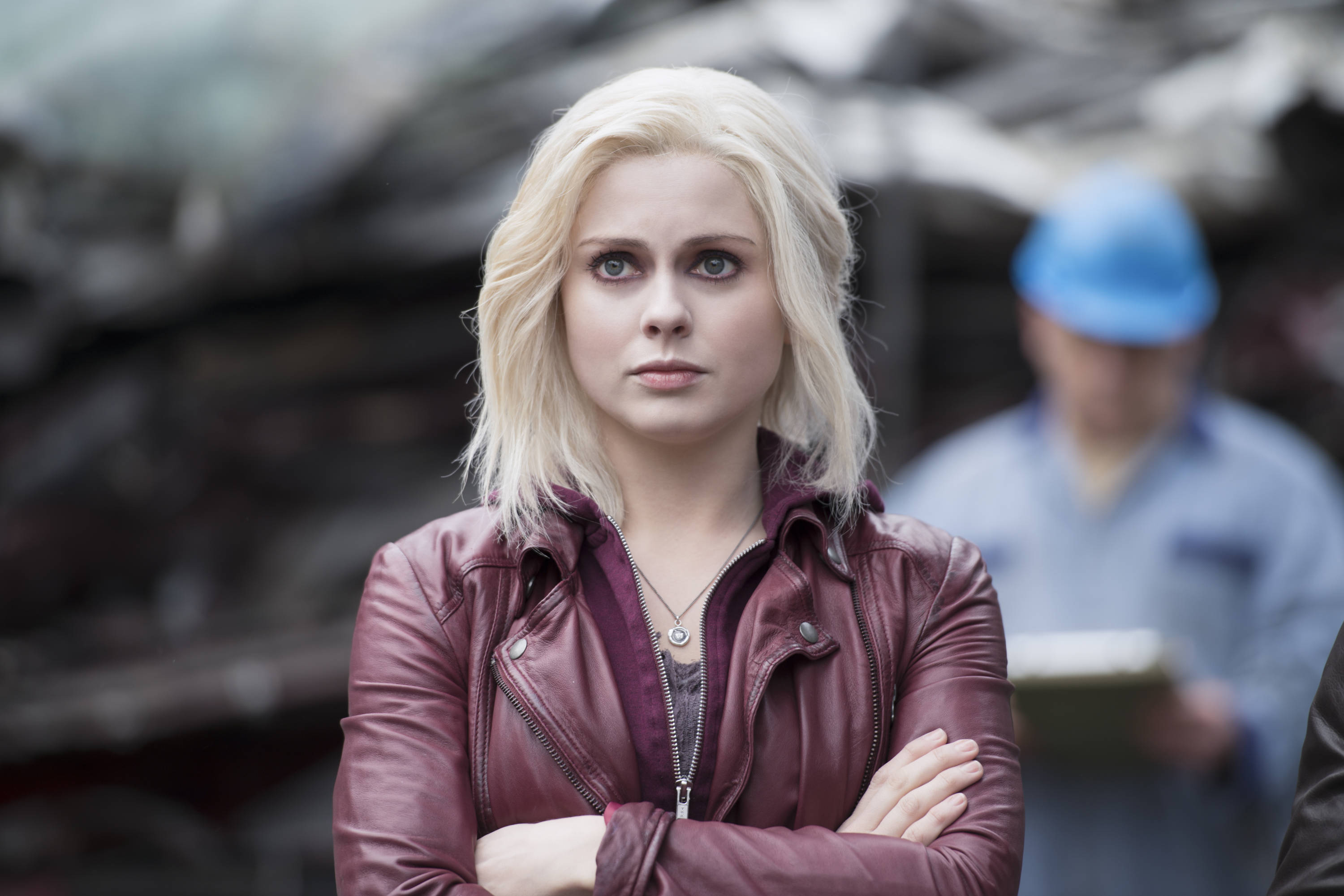《iZombie》莉芙·摩爾身穿紅色皮夾克 壁紙 — 一位金髮女子身穿栗色皮褸，雙手交叉，背景是模糊的工業場景。