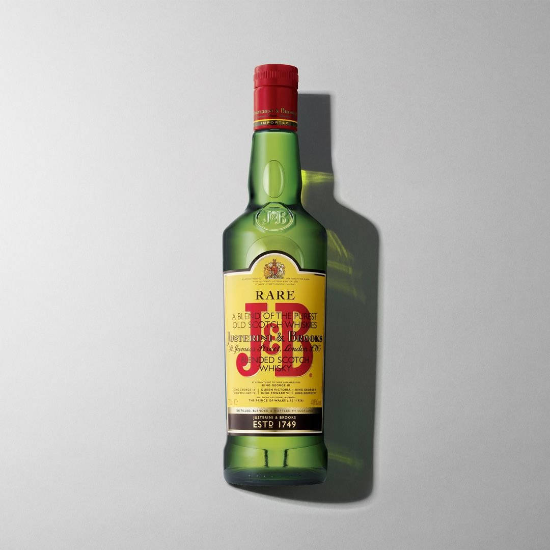 J&B Rare 威士忌瓶的經典風貌 壁紙 — 一個帶有紅色蓋子的J&B Rare調和蘇格蘭威士忌綠色玻璃瓶，立在純灰色背景前，投射出清晰的陰影。
