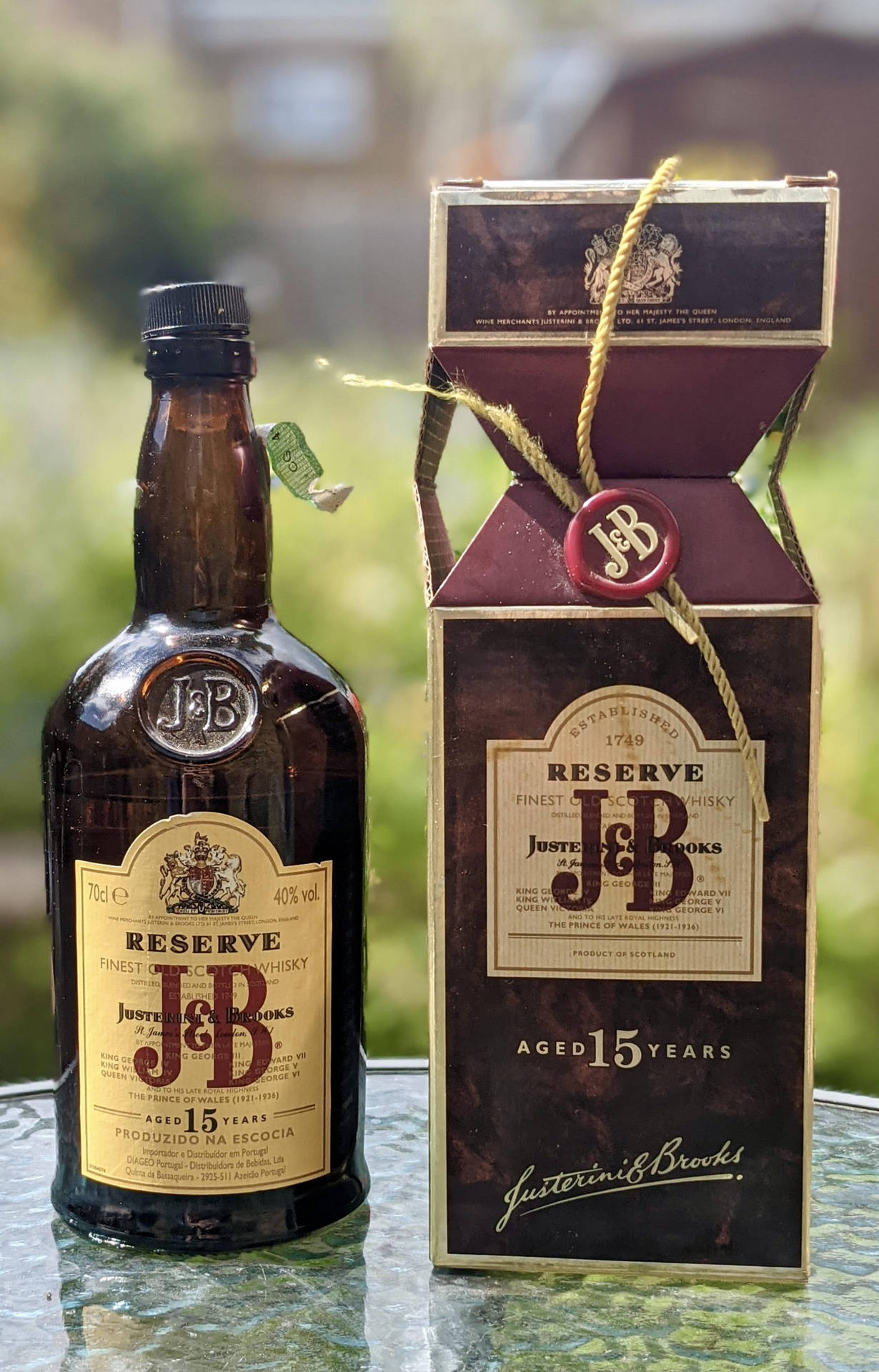 一瓶J&B Reserve 15年威士忌和盒子放在戶外的玻璃桌上。