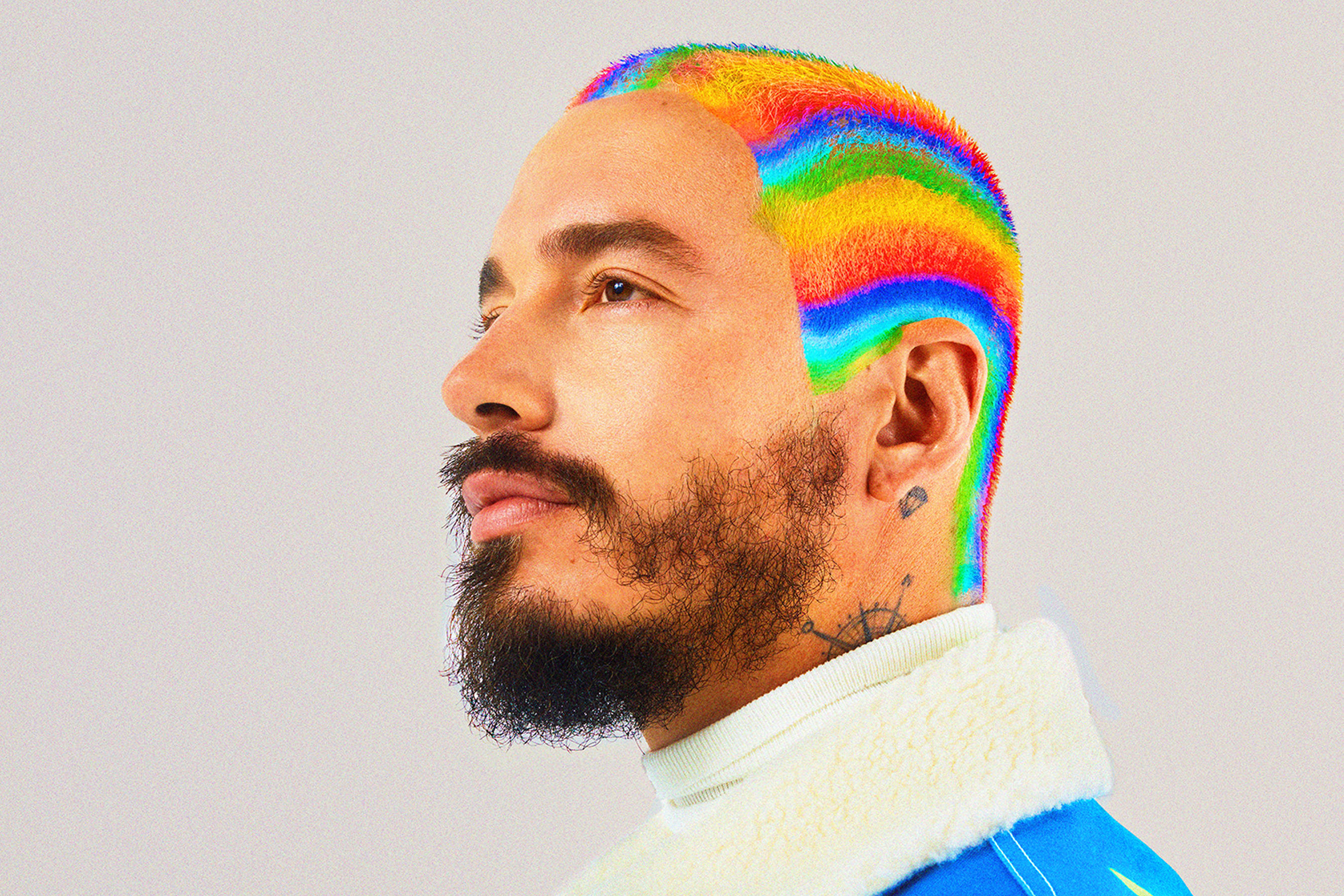 J Balvin 雨虹髮色 壁紙 — 一個擁有充滿活力的彩虹色髮型的男人，在純灰色背景前若有所思地凝視。