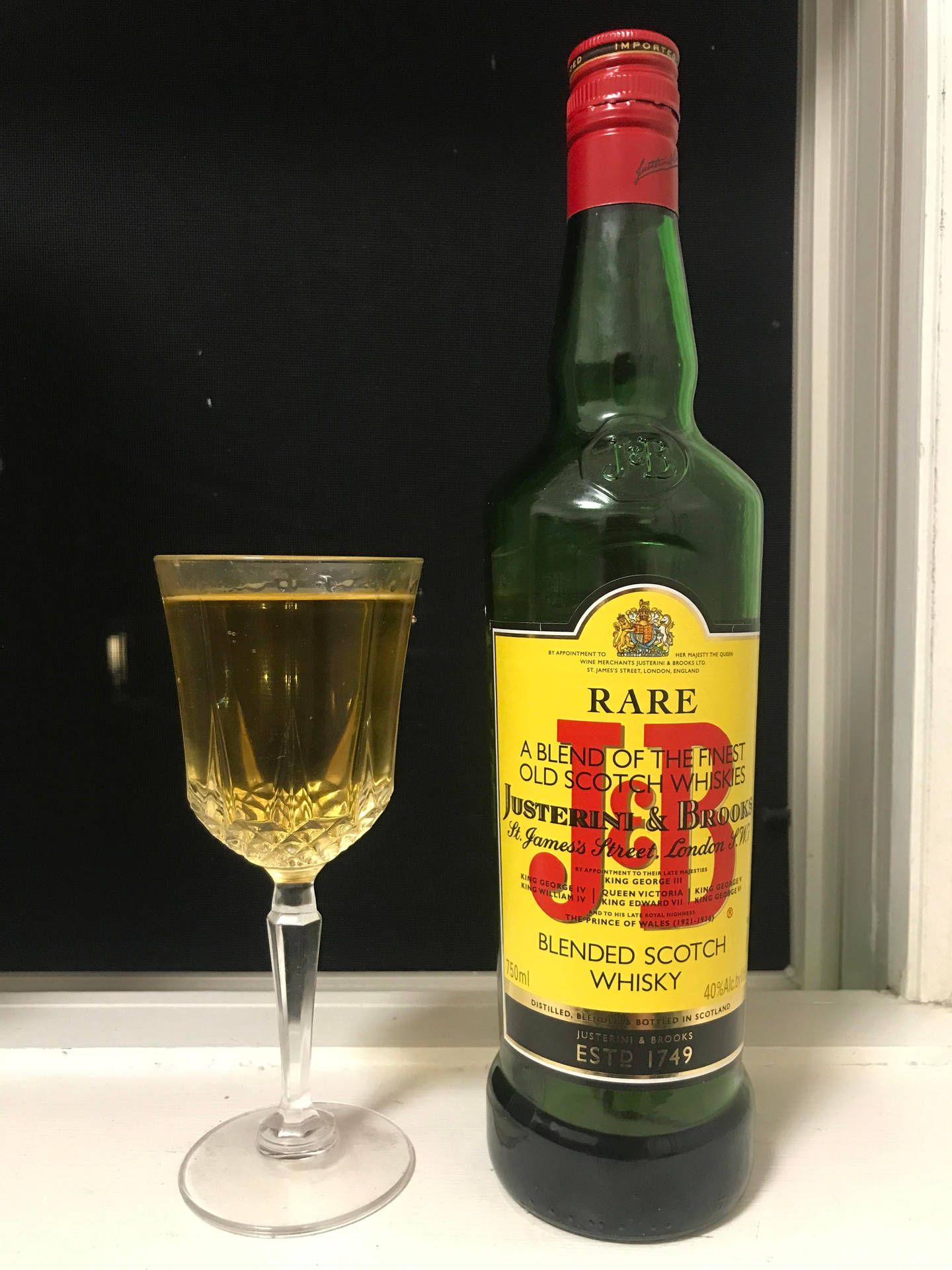 一瓶J D Rare威士忌旁邊放著一個裝滿酒的杯子在窗台上。