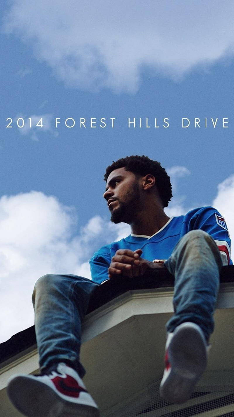 J Cole《2014 Forest Hills Drive》專輯封面 壁紙 — 一個穿著藍色球衣的年輕男子坐在屋頂邊緣，背景是明亮的藍天和蓬鬆的白雲。
