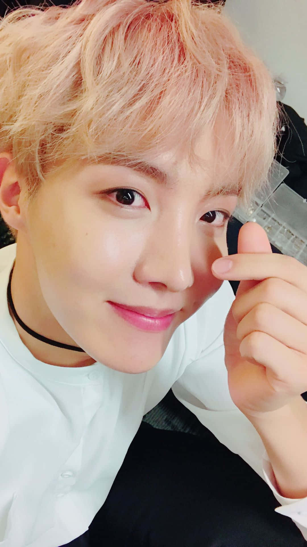J-hope BTS 指心 壁紙 — 粉紅色頭髮的年輕男子輕觸臉頰溫柔微笑的特寫自拍。