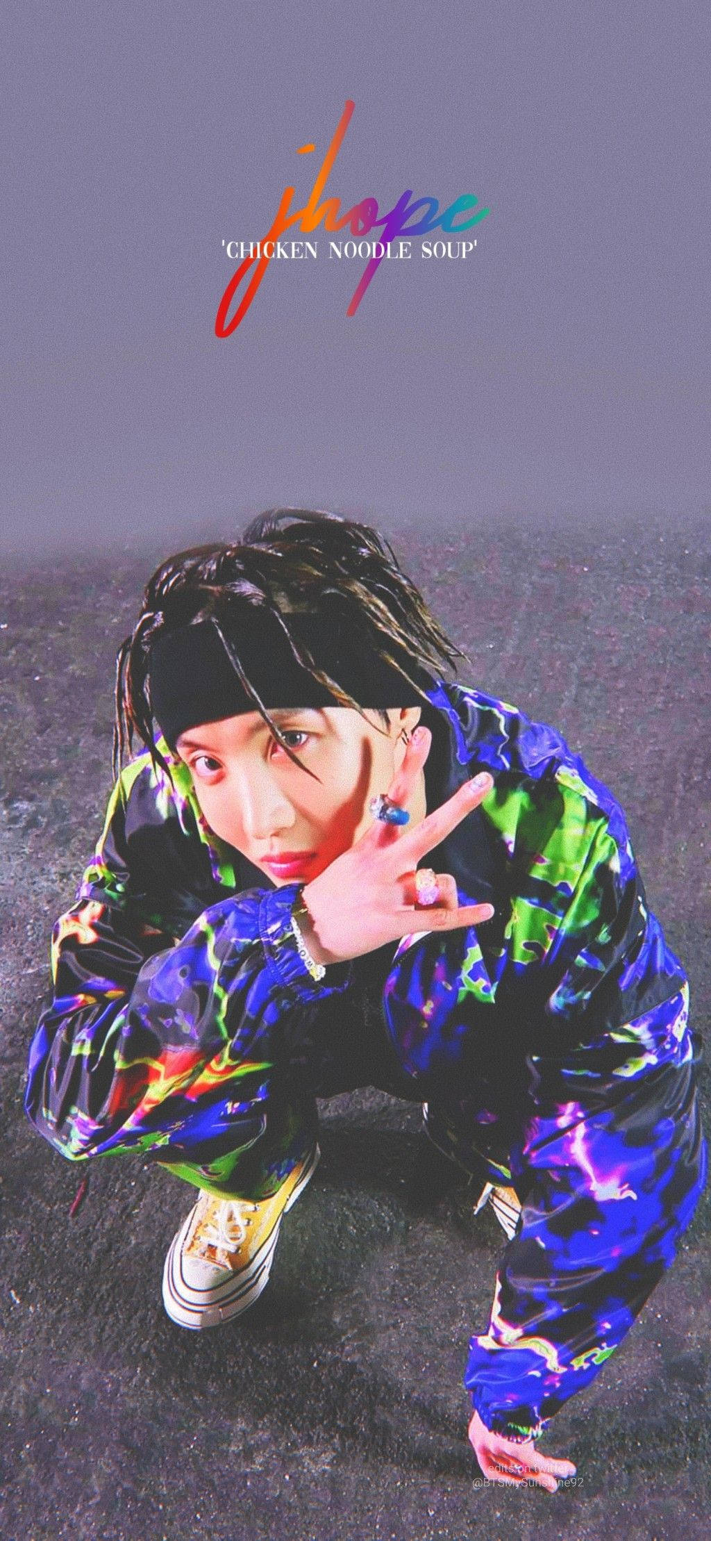 J-Hope《雞湯麵》宣傳照 壁紙 — 一名身穿鮮豔紮染外套的年輕男子蹲下，在深色紋理背景前比出和平手勢。