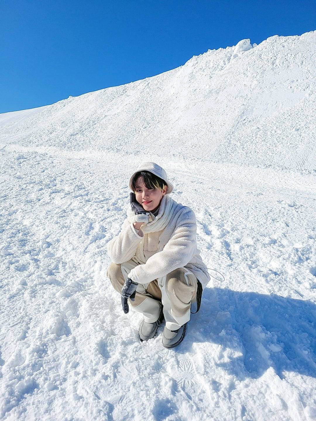穿著冬季服裝的人蹲在深雪中，頭頂是晴朗的藍天。