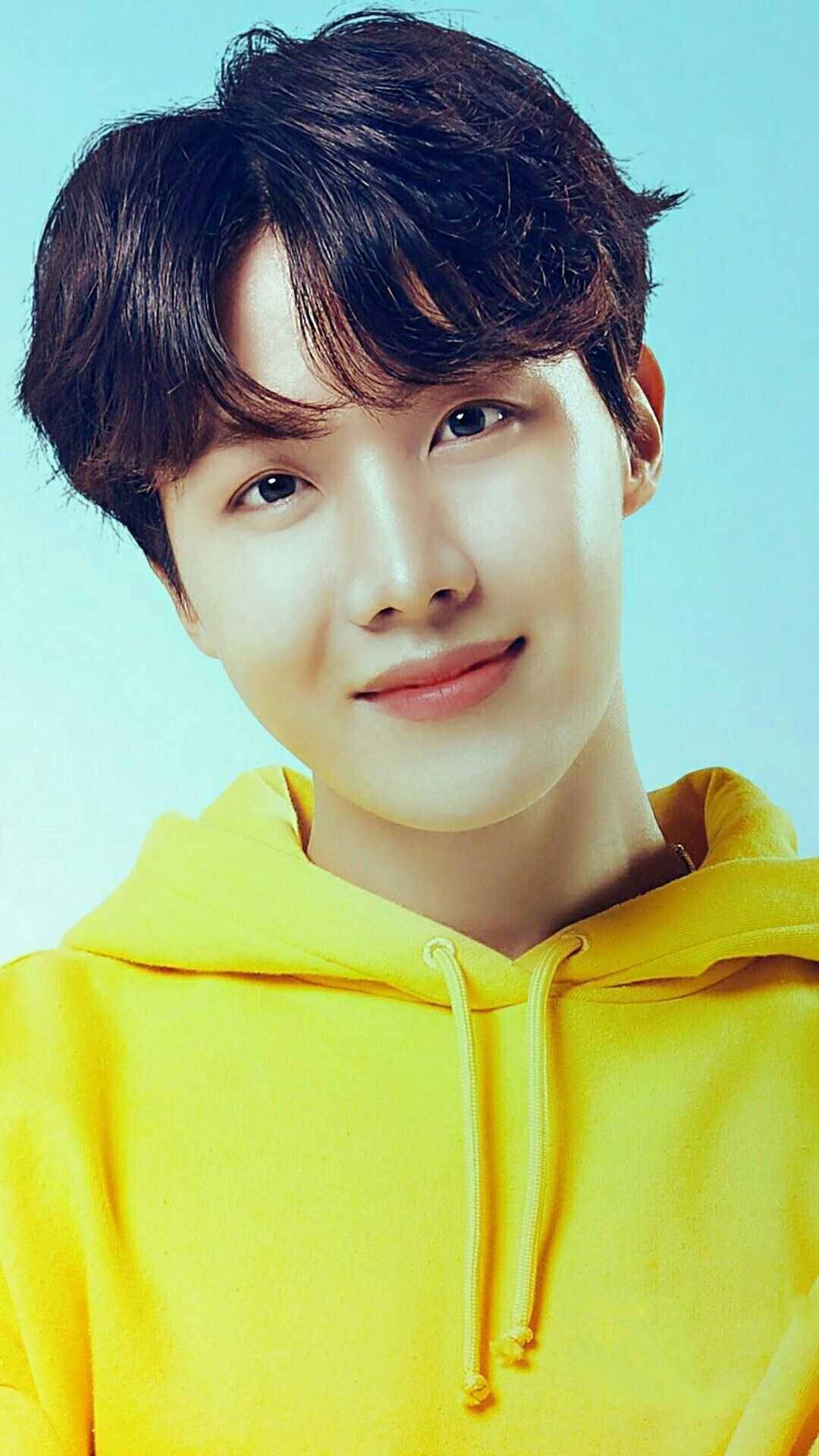 年輕男子穿黃色連帽衫在藍色背景前對鏡頭微笑