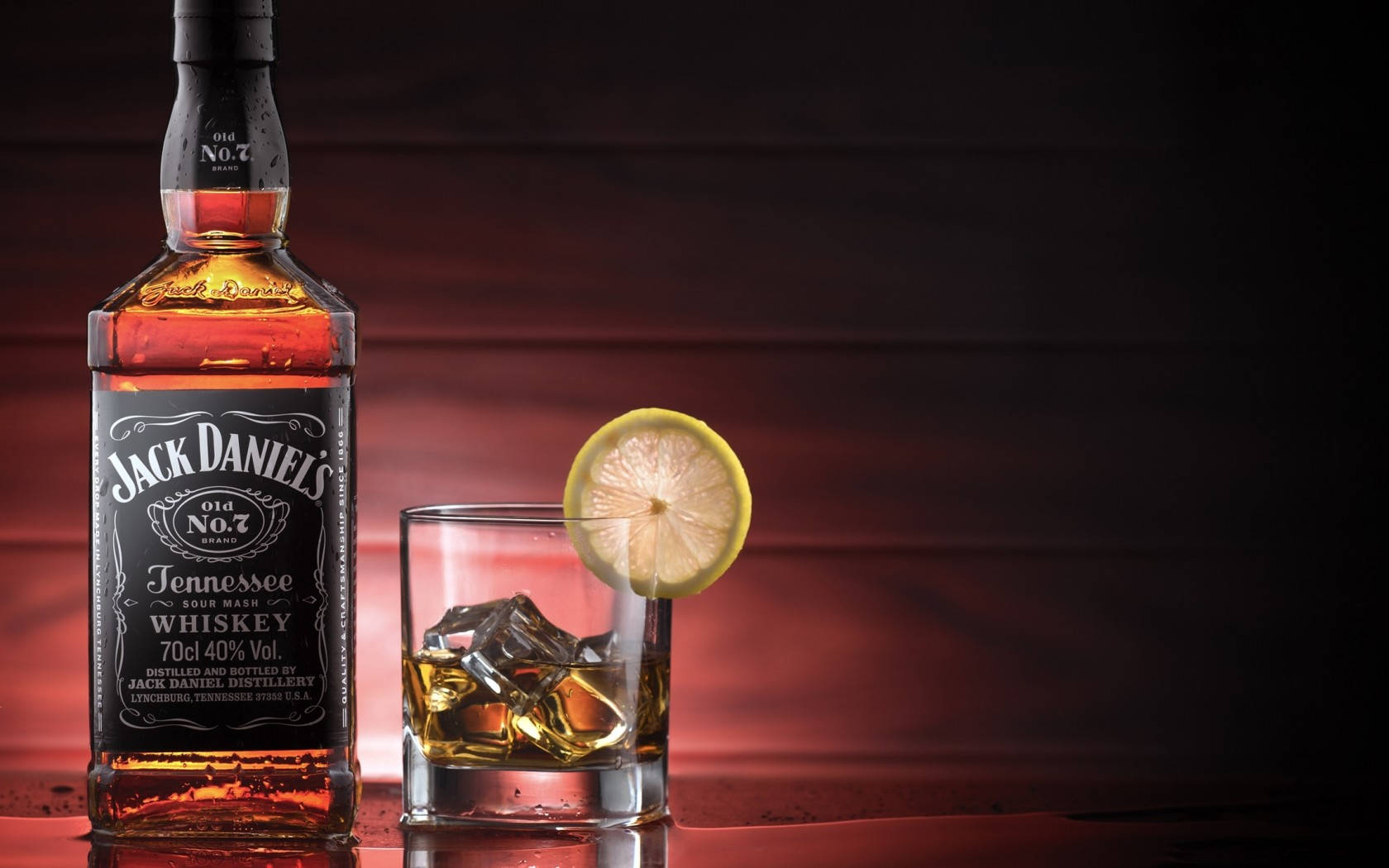 Jack Daniel's威士忌酒杯酒吧飲品 壁紙 — 一瓶Jack Daniel's威士忌和一杯加冰和檸檬片的玻璃杯在溫暖的紅色燈光下閃耀。