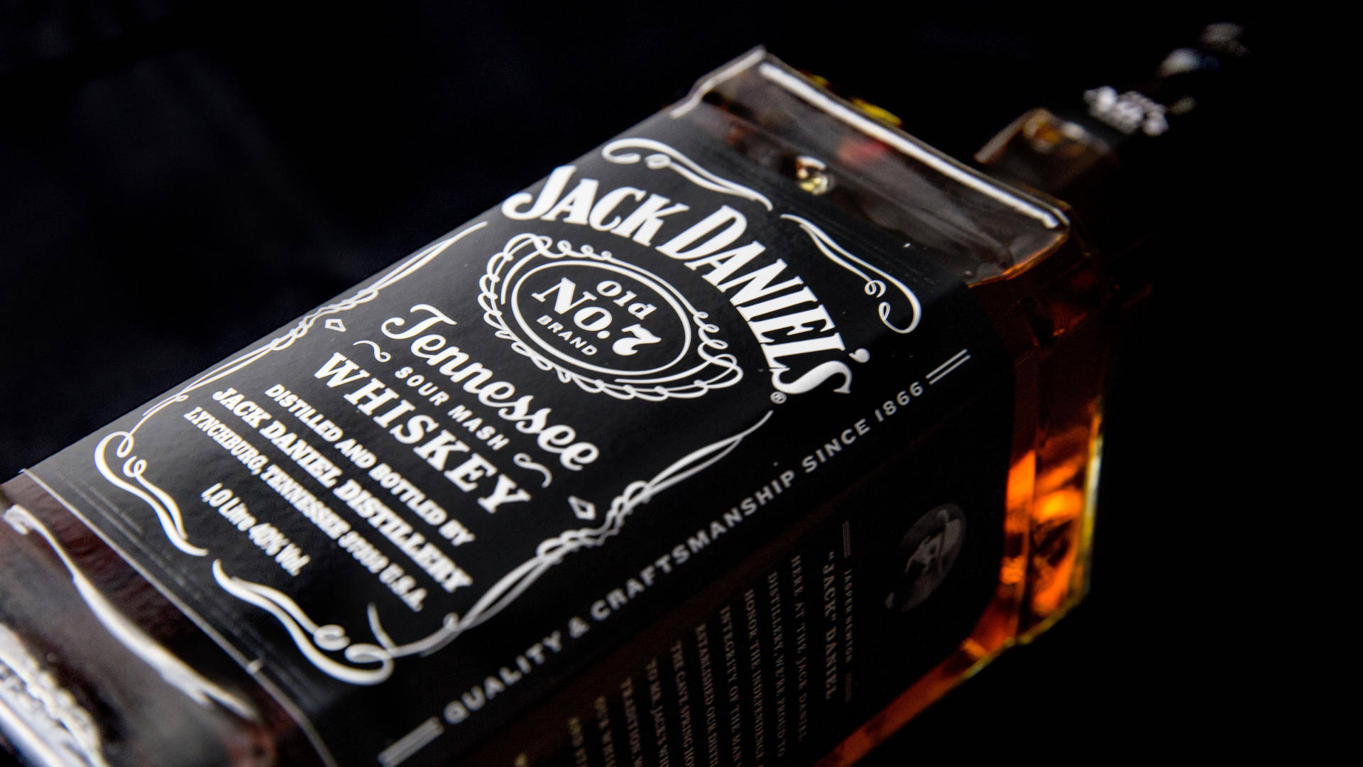 Jack Daniel's 威士忌酒瓶，琥珀色液體在黑暗背景下發光。