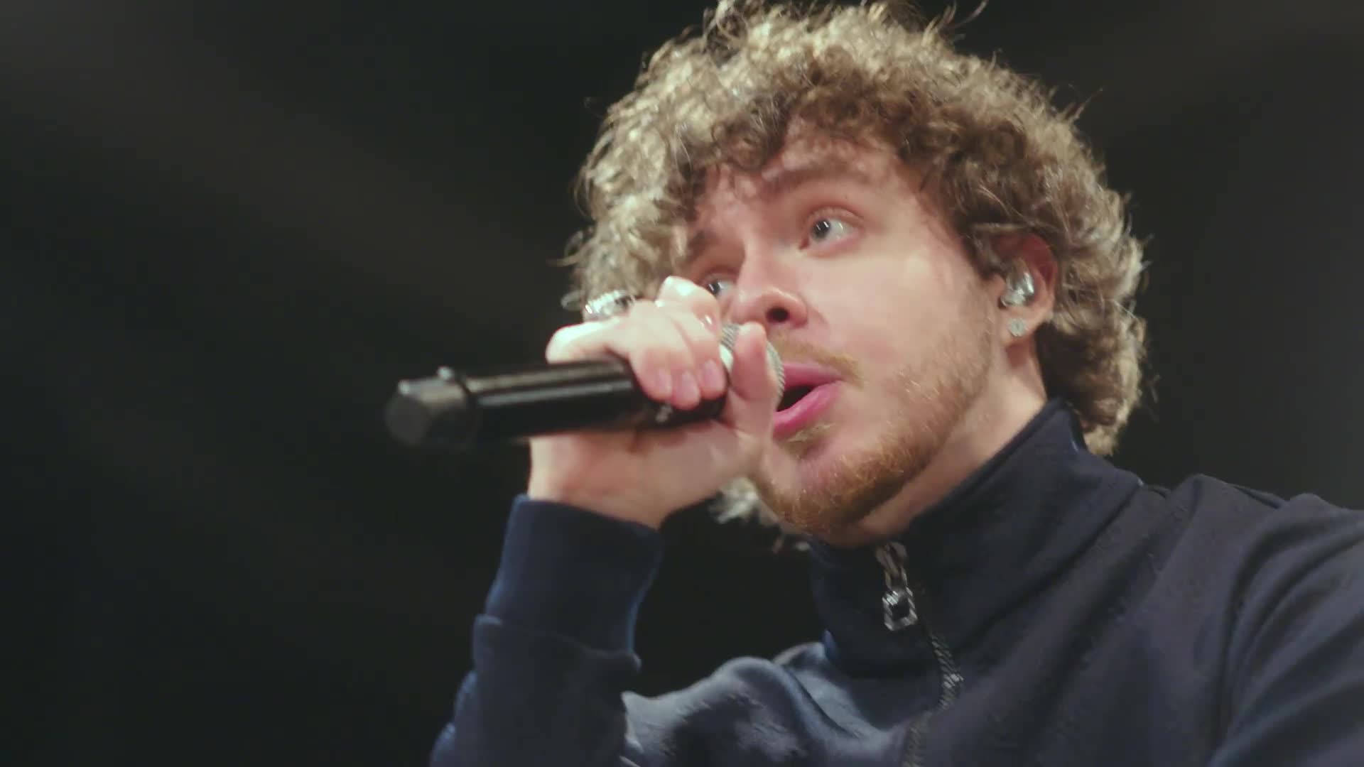 Jack Harlow 唱歌 壁紙 — 一位捲髮男歌手在舞台燈光下熱情地對著麥克風演唱。