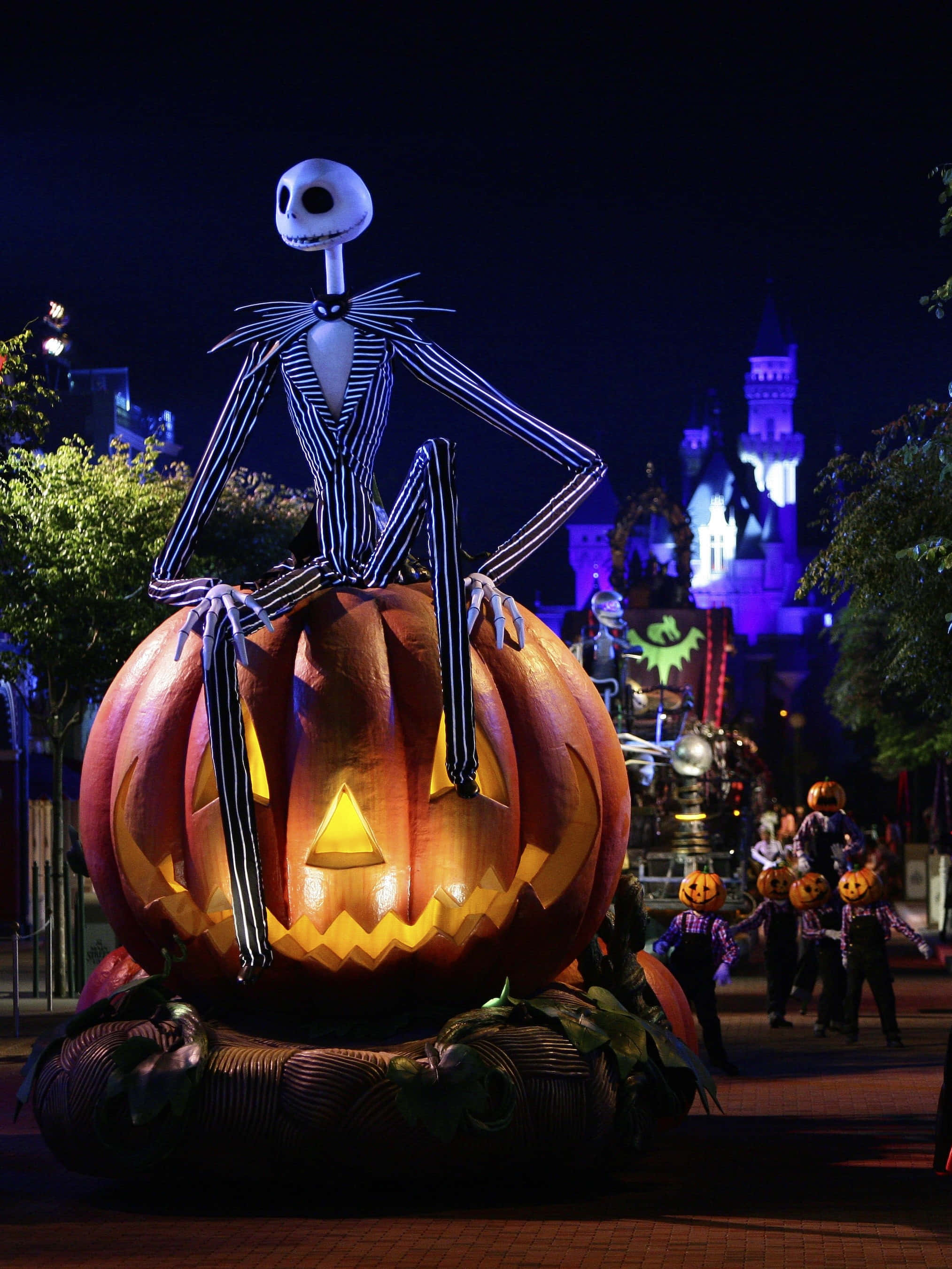 迪士尼萬聖節 桌布 壁紙 — Jack Skellington 喺夜晚嘅萬聖節巡遊中，坐喺一個巨大發光嘅南瓜上面，背景有城堡燈光。