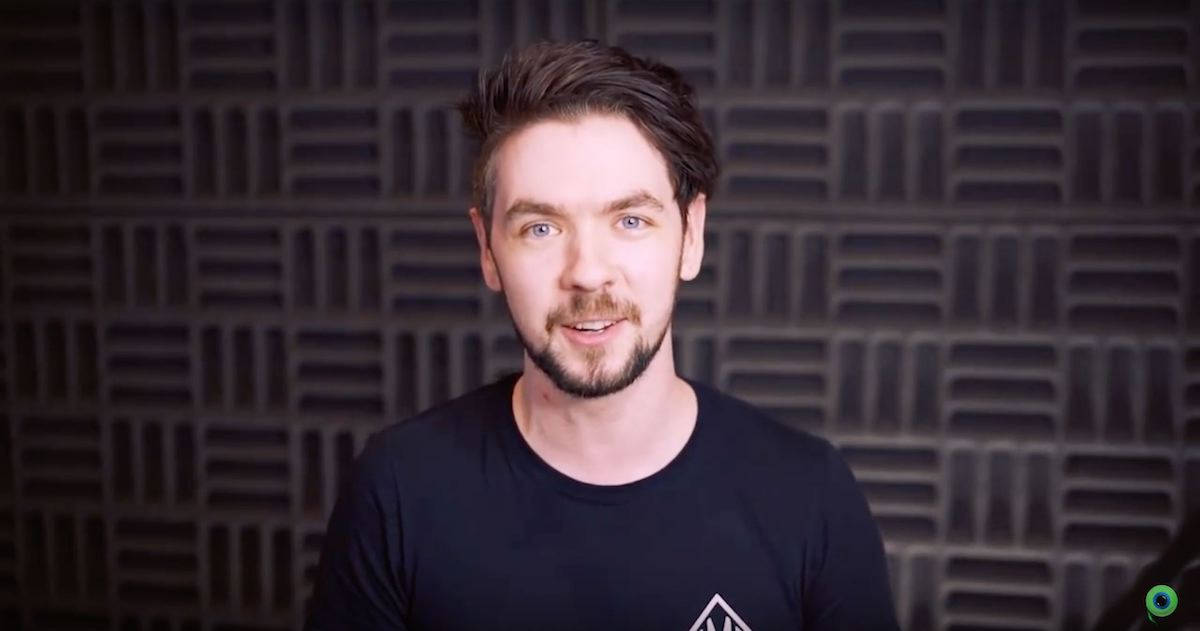 Jacksepticeye YouTube 影片開場 壁紙 — 一個藍眼睛、留鬍鬚的男人在深色幾何聲學牆前對著鏡頭微笑。