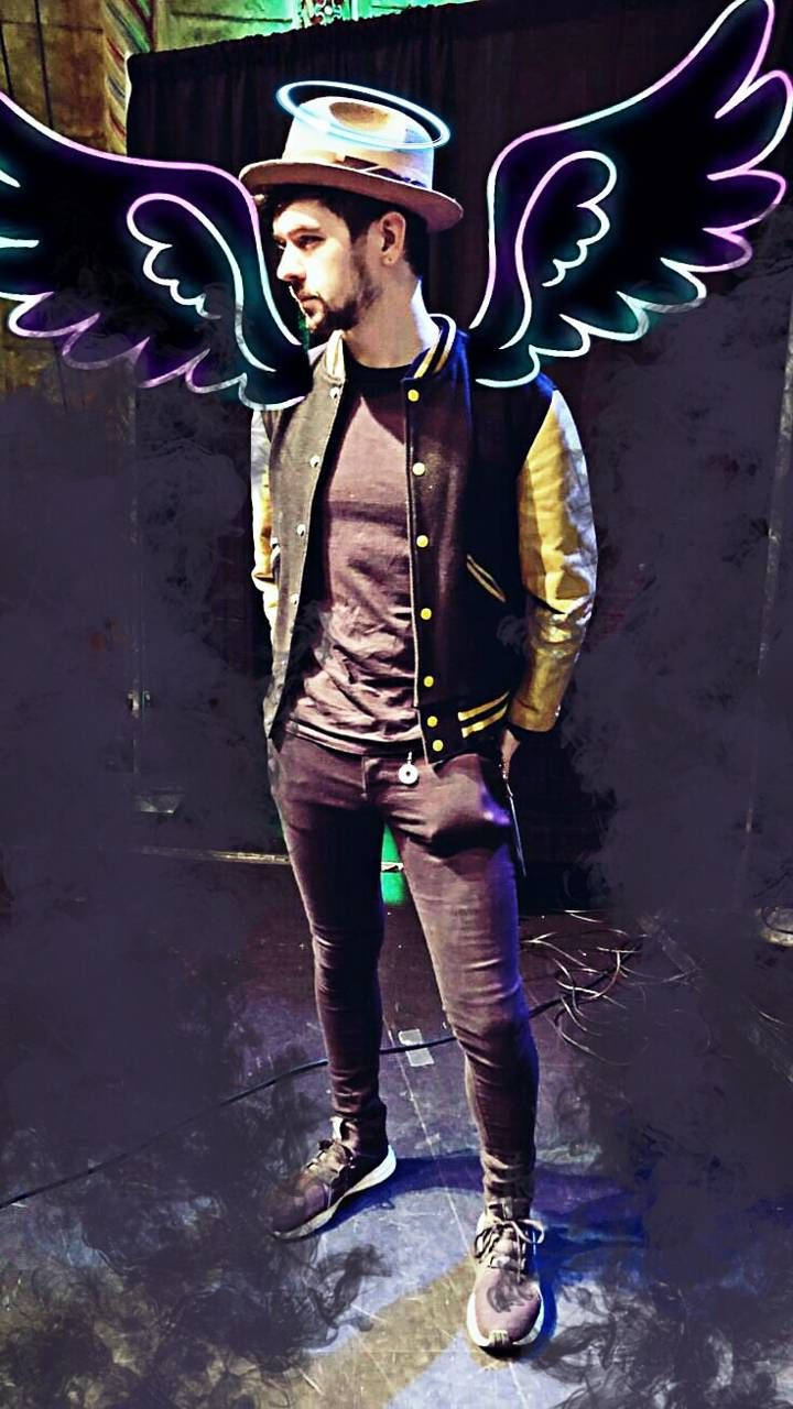 Jacksepticeye 天使塗鴉風格 壁紙 — 一個戴著紳士帽和校隊夾克的男人，在黑暗背景下站著，擁有發光的霓虹天使翅膀。