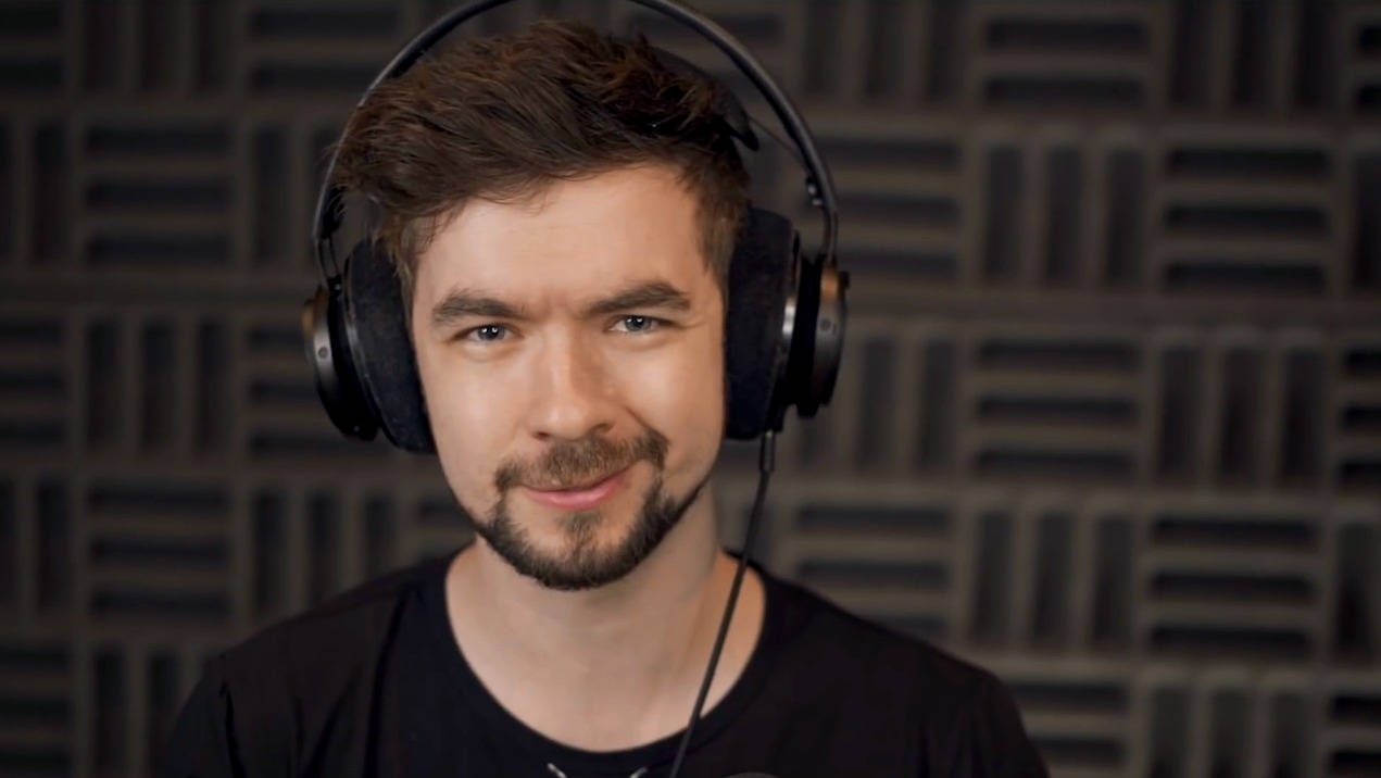 Jacksepticeye 微笑瞬間 壁紙 — 一位留鬍鬚、戴耳機的男子在深色隔音板牆前對著鏡頭微笑。
