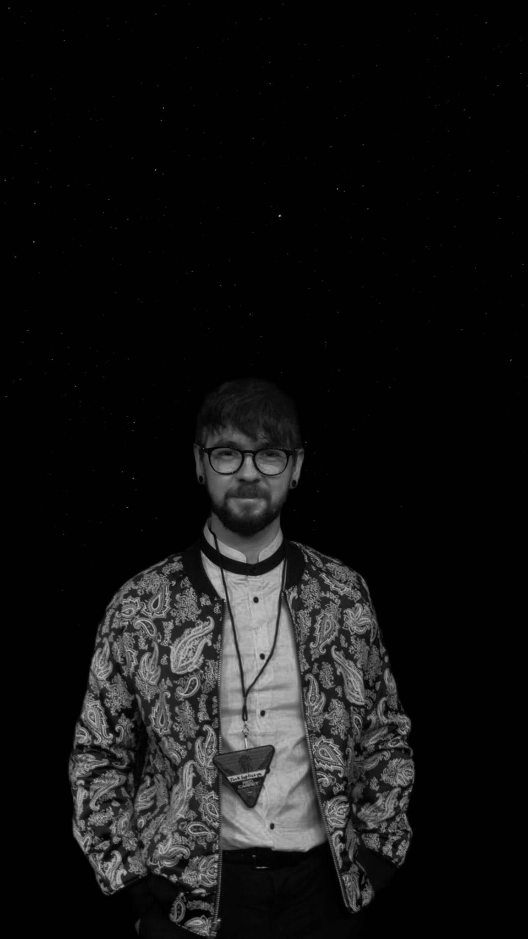 Jacksepticeye 黑白星夜 壁紙 — 一個戴眼鏡、身穿圖案外套的男人，站在單色的星空夜空下。