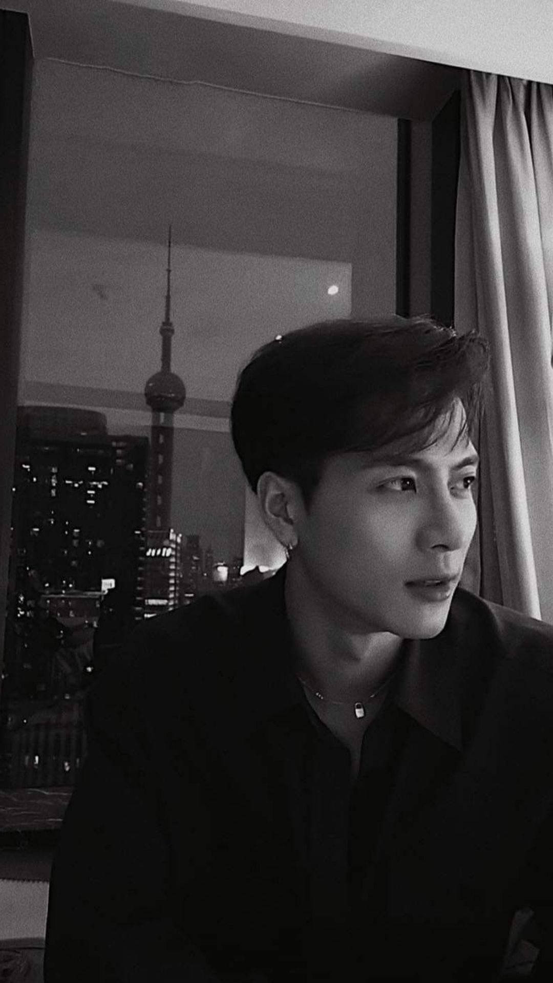 Jackson Wang 偷拍美照 壁紙 — 一個年輕男子若有所思地望向窗外，欣賞夜晚燈火璀璨的上海天際線。