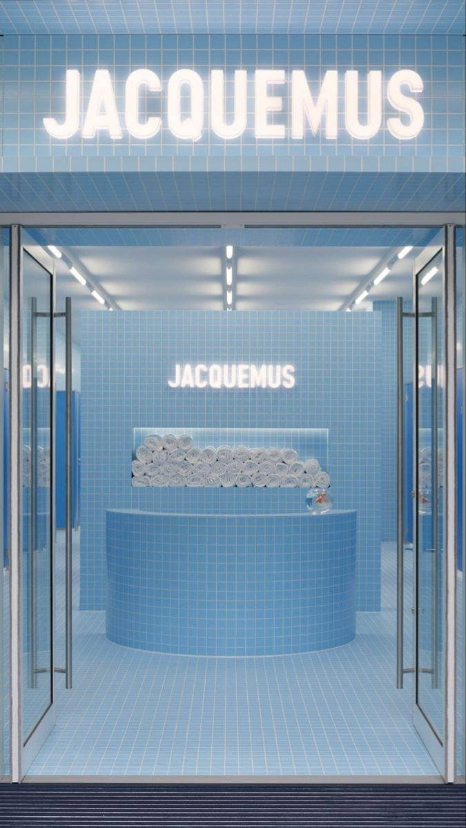 嬰兒藍 Jacquemus 店鋪 壁紙 — Jacquemus 店舖內部採用極簡風格，配以藍色瓷磚、發光標誌和一個中央底座，上面放有捲起的毛巾。
