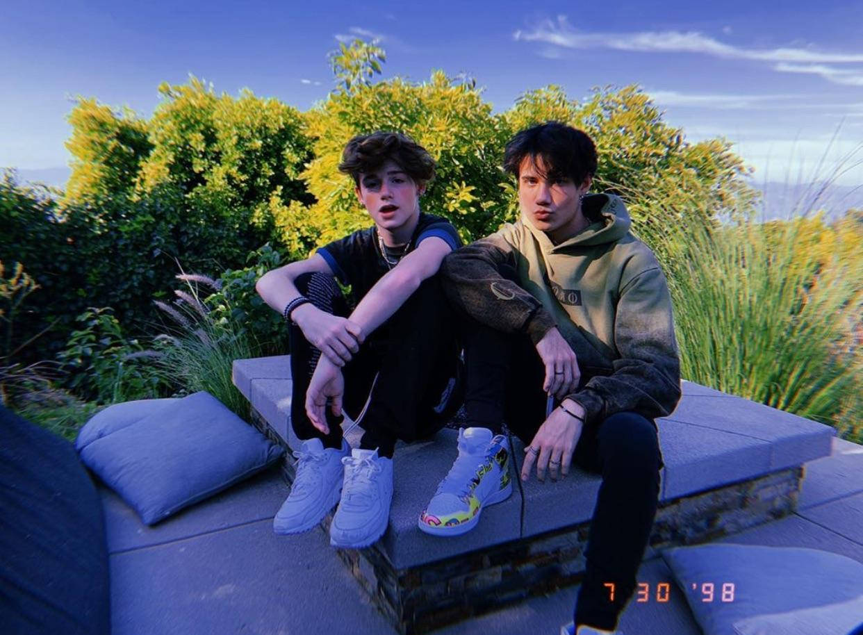 Jaden Hossler 與 Payton Moormeier 壁紙 — 兩名年輕男子在晴朗藍天下，隨意坐在被茂密綠植環繞的石凳上。