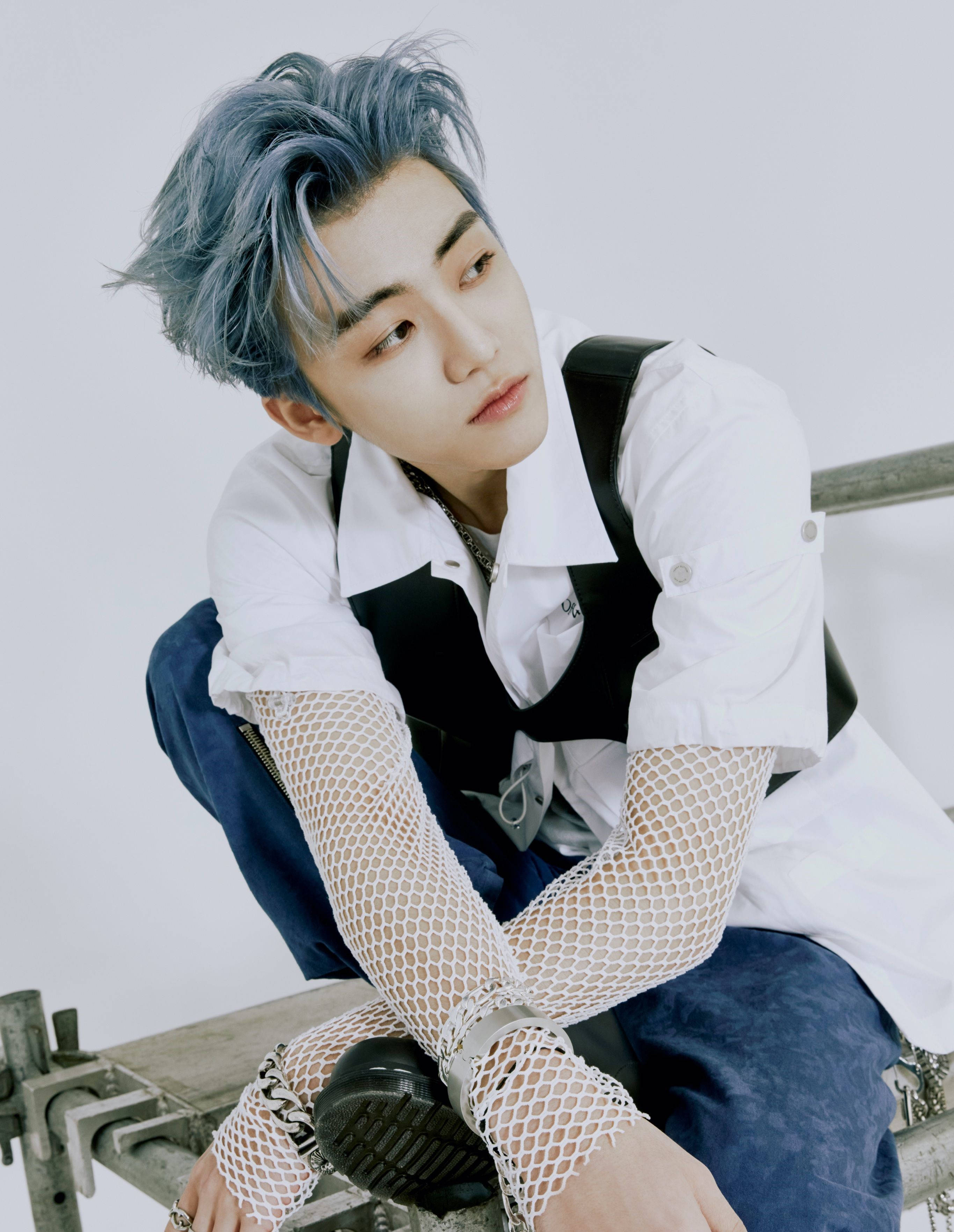 Jaemin NCT 魚網袖 壁紙 — 一位藍髮年輕男子坐在金屬長椅上，身穿白色襯衫、黑色背心和漁網袖套，背景為純白色。