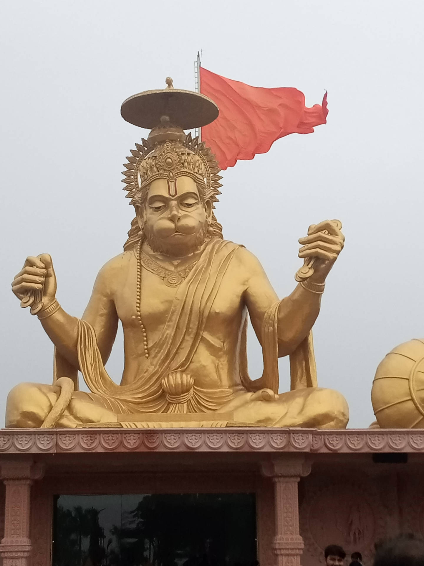 金色哈努曼雕像坐在寺廟平台上，紅旗飄揚。