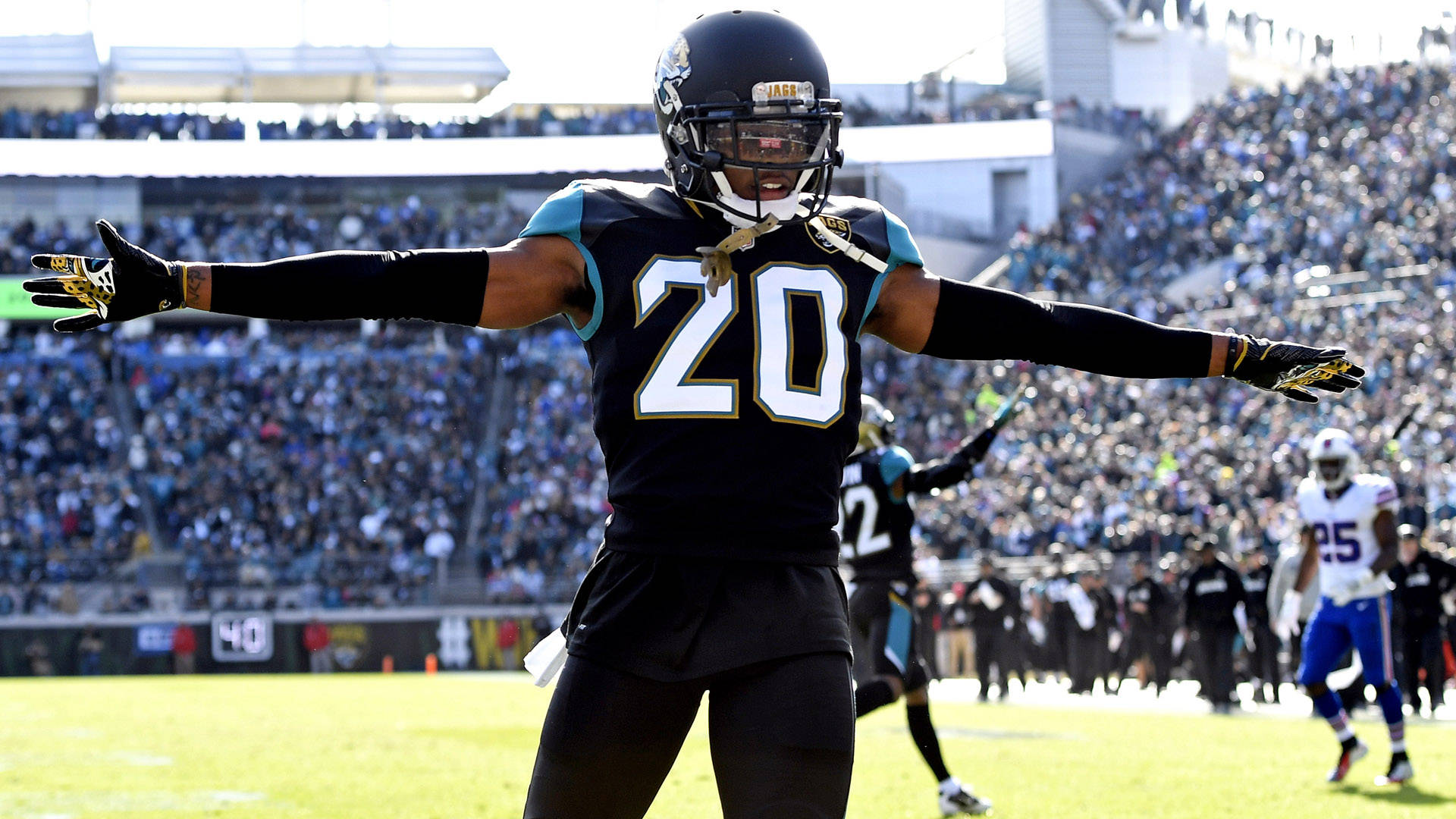 Jalen Ramsey 在 AFC 野生卡比賽 壁紙 — 一名身穿黑色和青綠色球衣、號碼20的傑克遜維爾美洲虎隊美式足球員，在陽光明媚的球場上張開雙臂慶祝，面前是座無虛席的體育場。