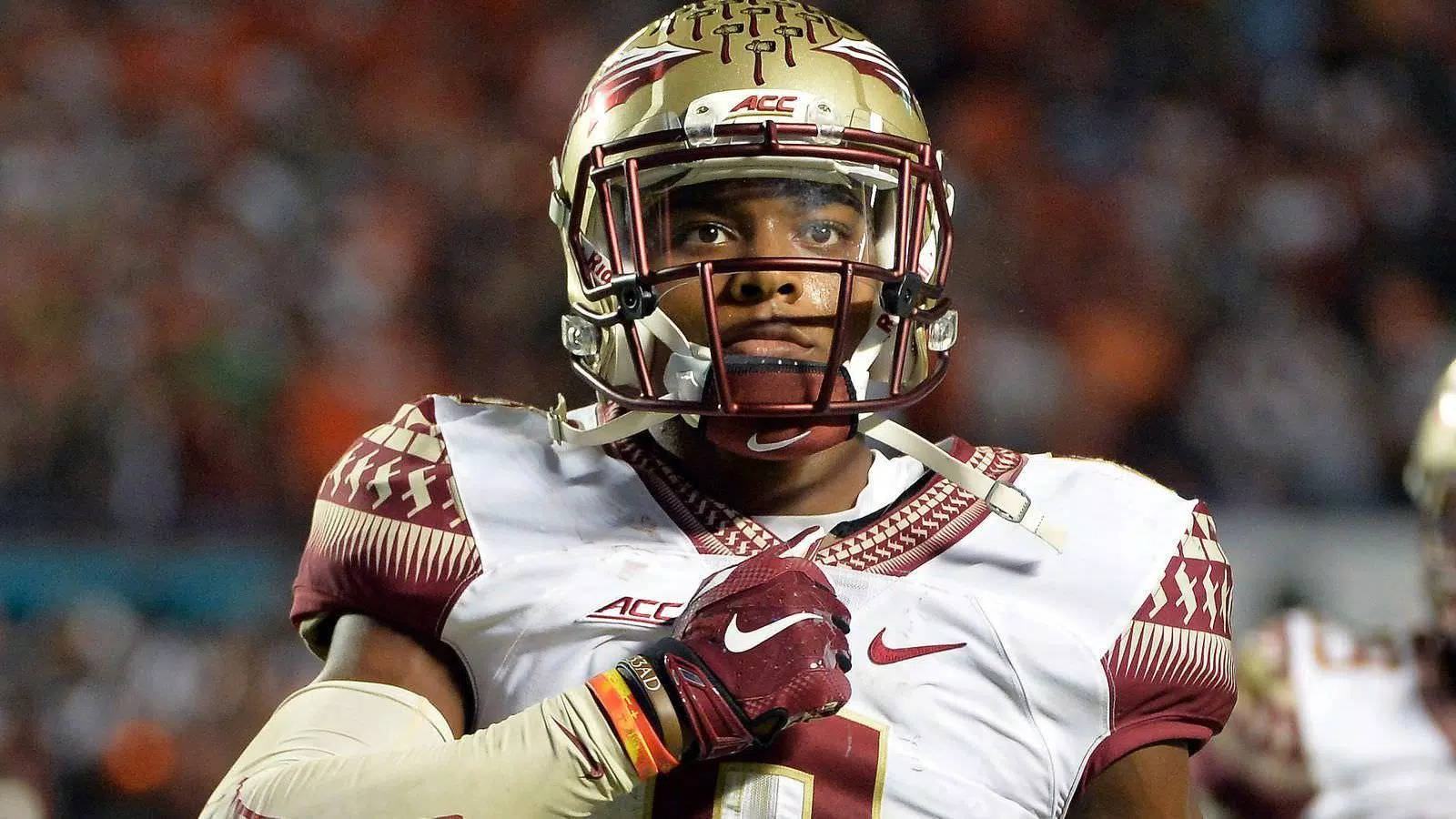 Jalen Ramsey 佛羅里達州立大學 壁紙 — 一名專注的美式足球員身穿栗色和金色制服，在夜間比賽的體育場燈光下凝視前方。
