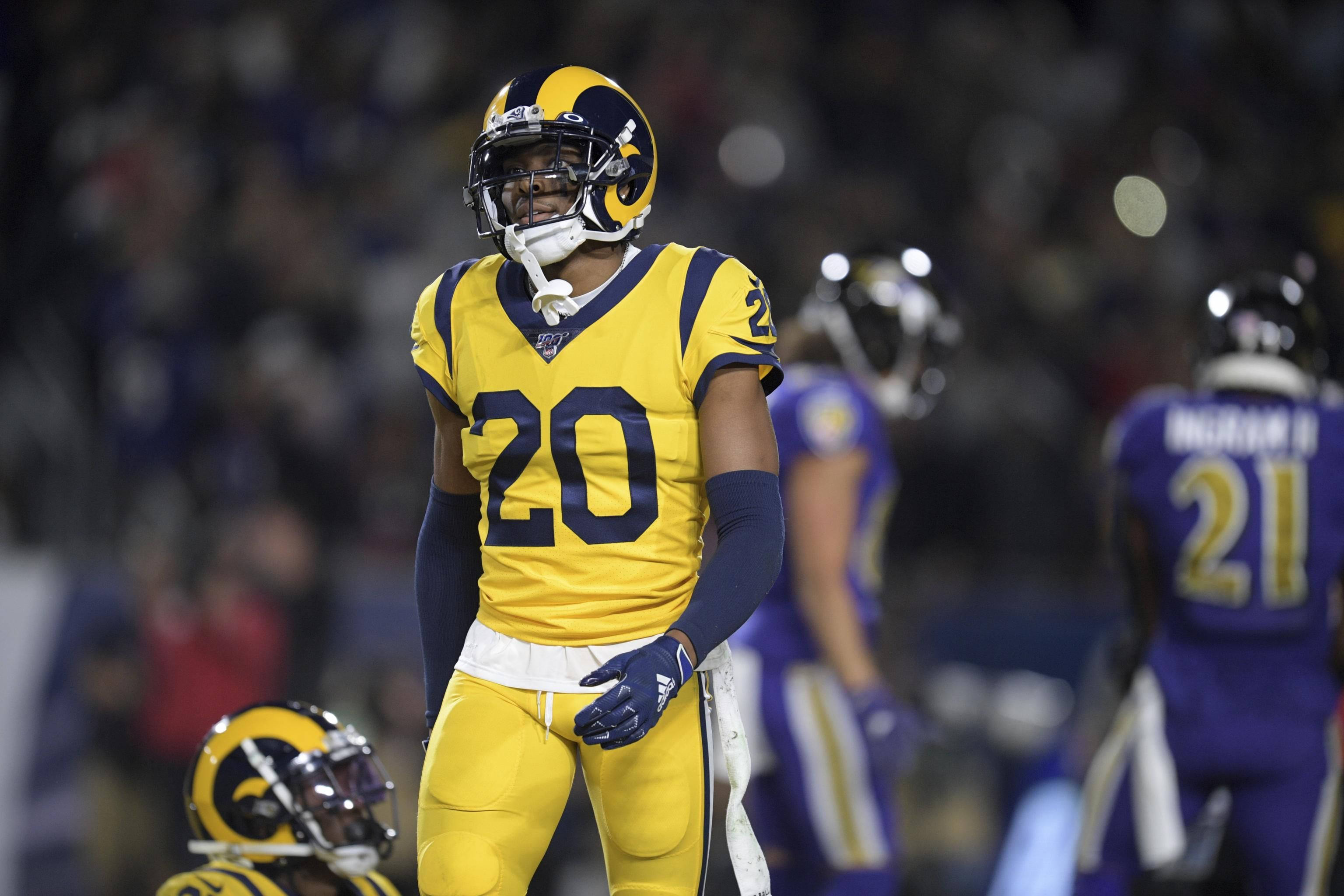 Jalen Ramsey 對戰巴爾的摩雷鳴隊 壁紙 — 一名身穿黃藍色球衣的洛杉磯公羊隊美式足球員在夜間比賽中專注地站在球場上，身後體育場燈光閃爍。