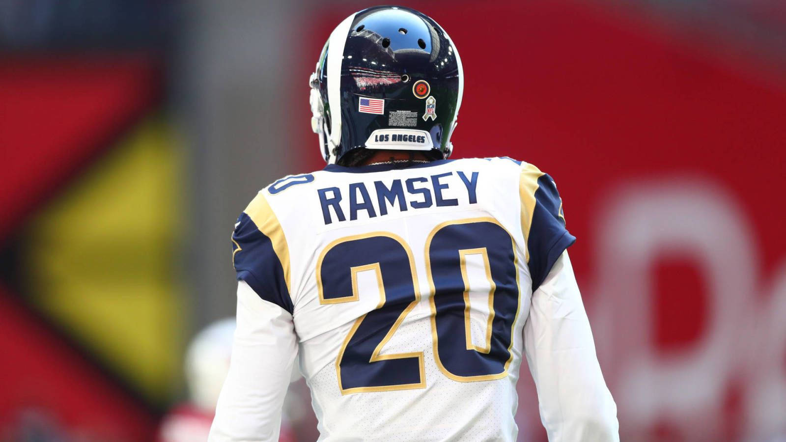 Jalen Ramsey 後側角度拍攝 壁紙 — 一名美式足球員身穿白色球衣，帶有藍色和金色點綴，背後印有名字Ramsey和20號，戴著頭盔站立。