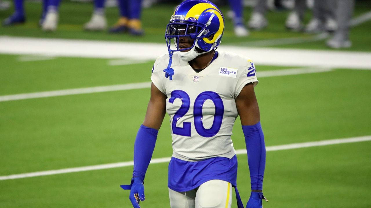 Jalen Ramsey 於FedEx體育場 壁紙 — 一位洛杉磯公羊隊的足球運動員穿著藍色和金色的裝備，在體育場燈光下走在綠色球場上。