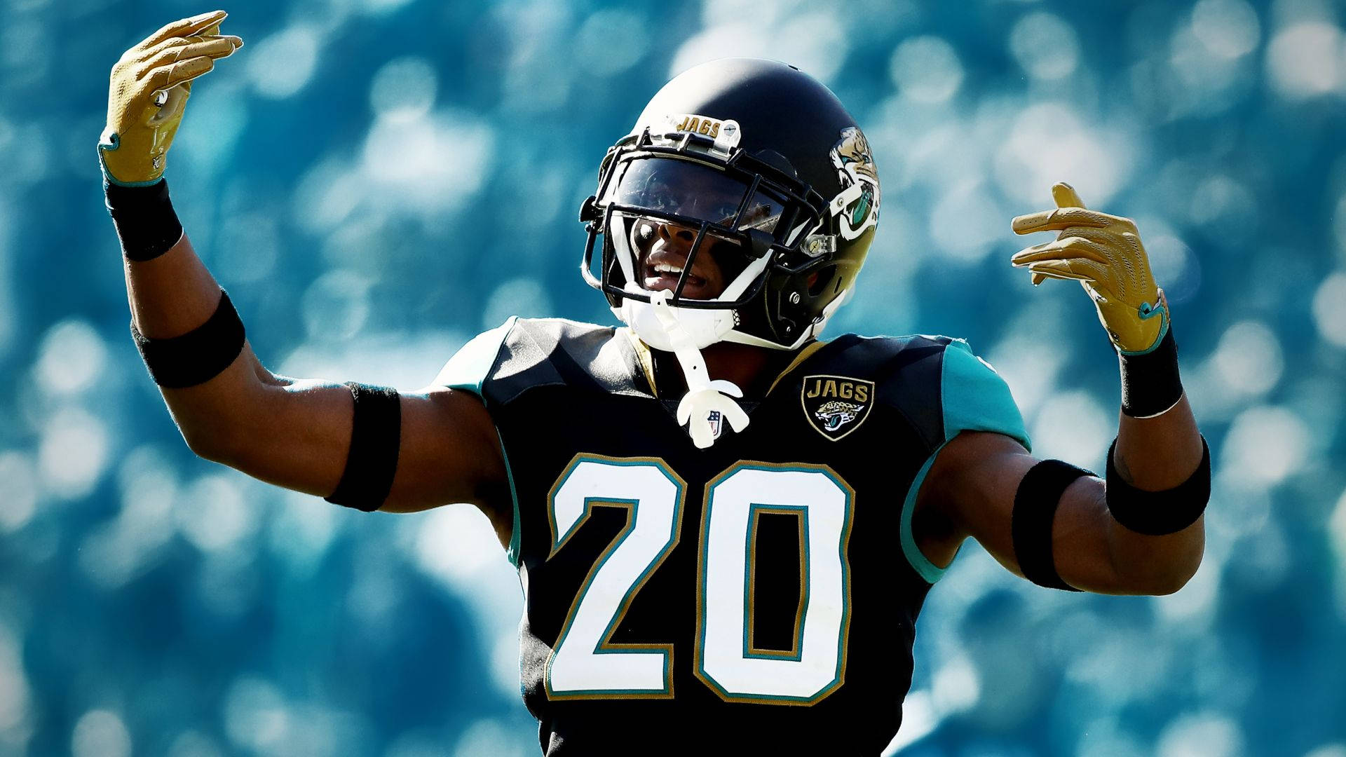 Jalen Ramsey 淡化背景 壁紙 — 一名傑克遜維爾美洲虎隊的足球運動員，身穿黑色和藍綠色球衣，號碼20，在模糊的體育場背景下舉臂慶祝。