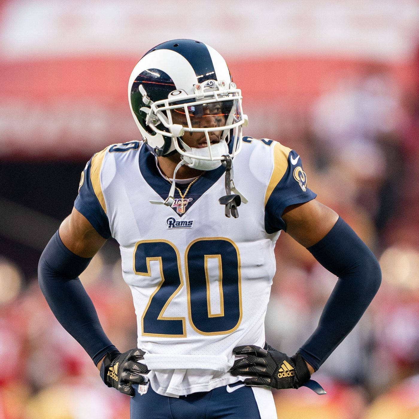 Jalen Ramsey 足球運動員 壁紙 — 一位專注的NFL美式足球員，身穿白色和金色的公羊隊20號球衣，雙手叉腰站在模糊的體育場地上。
