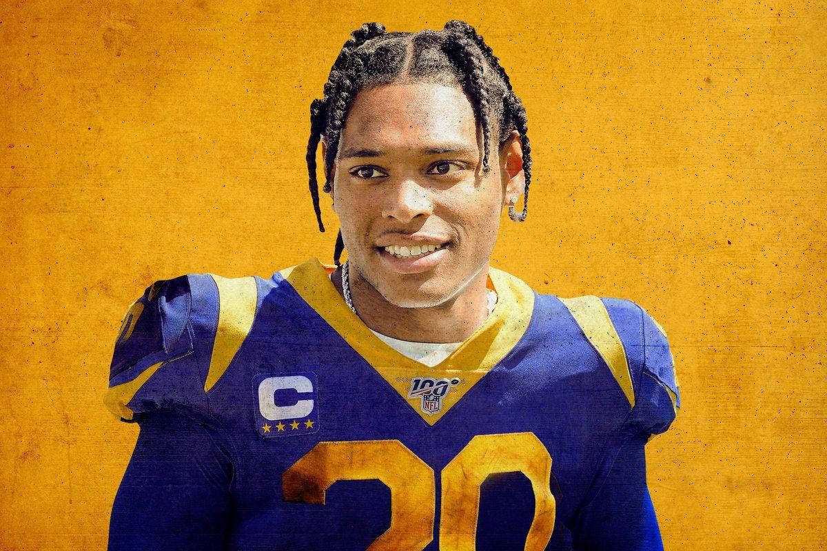 Jalen Ramsey 金色背景 壁紙 — 一位微笑的足球運動員，身穿藍色和金色的球衣，號碼20，帶有隊長臂章，背景是紋理黃色。
