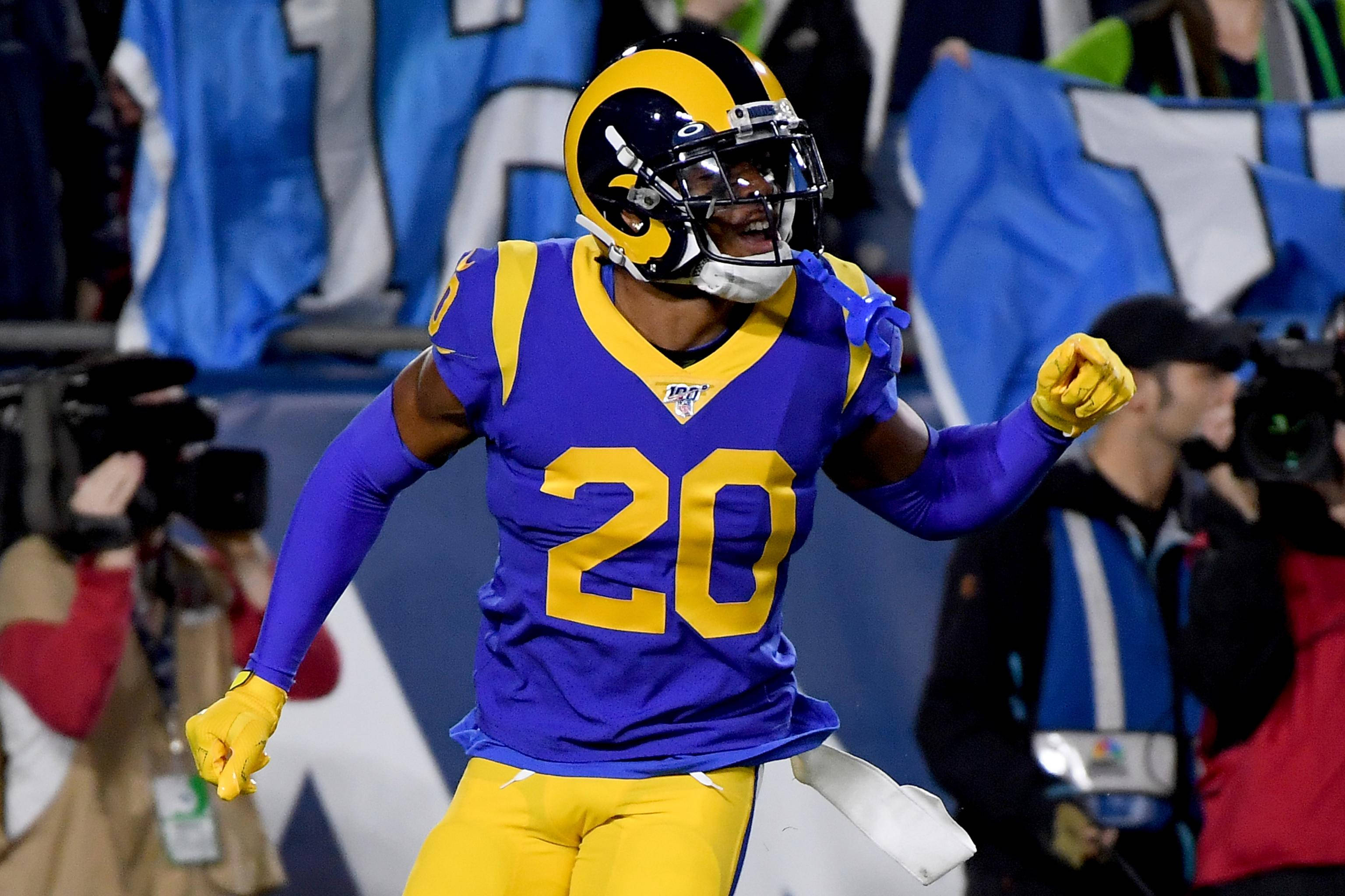 Jalen Ramsey 領唱瞬間 壁紙 — 一位身穿紫色和金色球衣、背號20的洛杉磯公羊隊美式足球員，在球場燈光下的一場比賽中舉起拳頭慶祝。