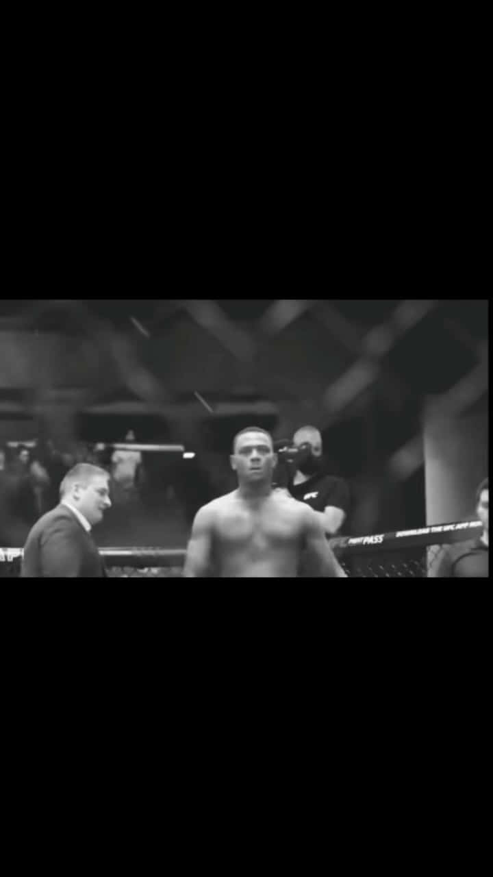 一名赤裸上身的MMA拳手在八角籠中面對一名西裝男。