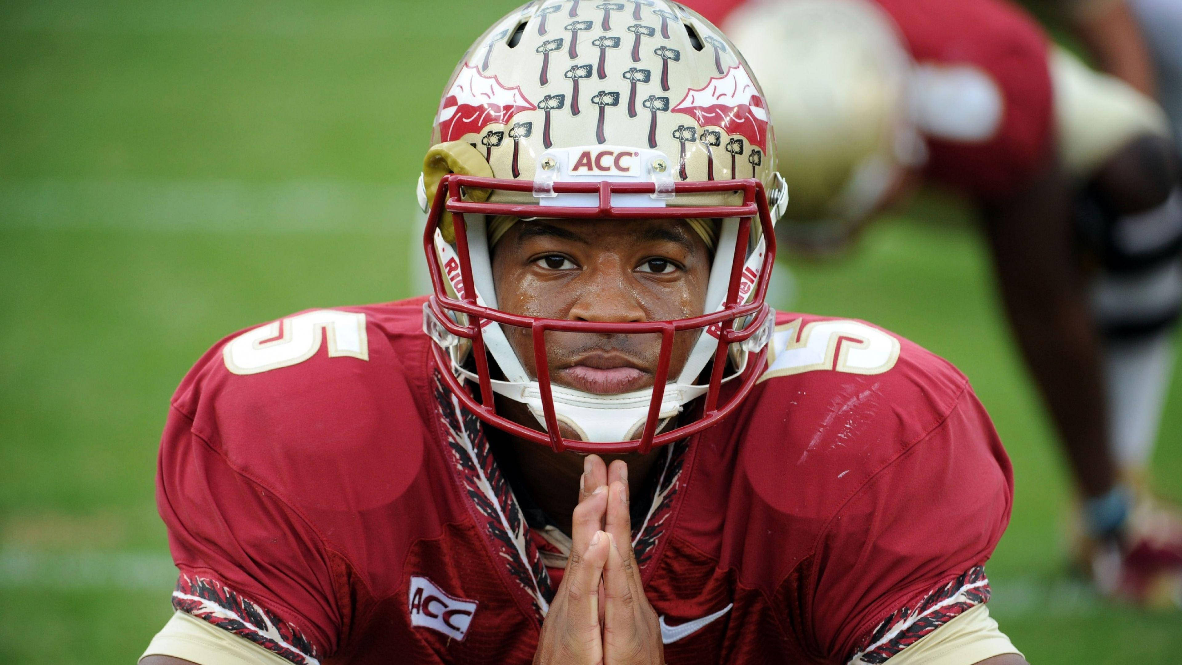Jameis Winston 足球賽場親眼對鏡 壁紙 — 一名專注的美式足球員身穿栗色制服，跪在綠色球場上，雙手在頭盔下緊握。