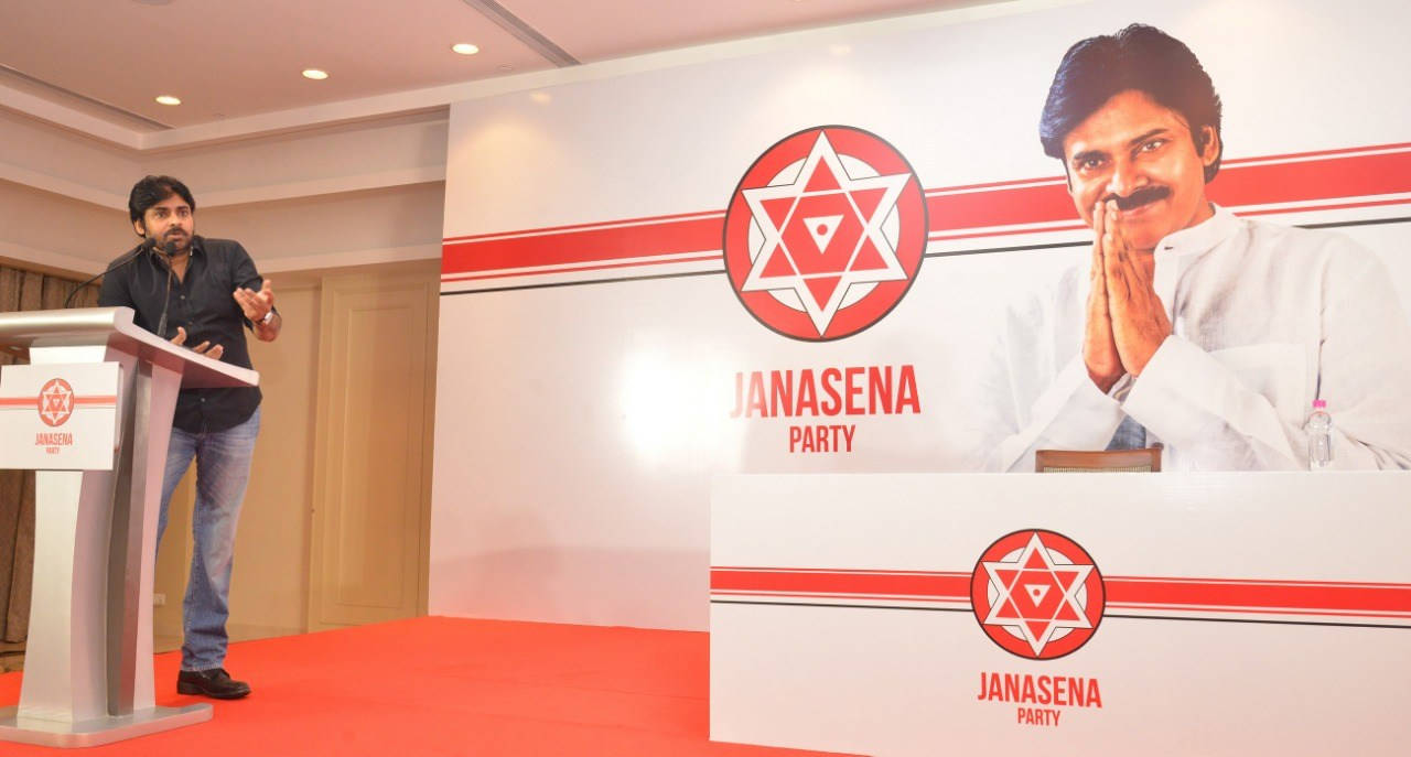 男子在Janasena Party活動中，在品牌背景前發表政治演講。