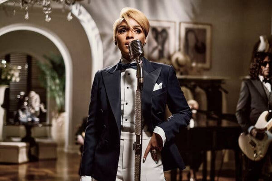 Janelle Monáe 舞台表演 x Ralph Lauren 壁紙 — 一位身穿海軍藍燕尾服的魅力歌手在溫暖燈光下、裝飾華麗的房間裡對著復古麥克風演唱，背景有一位結他手。