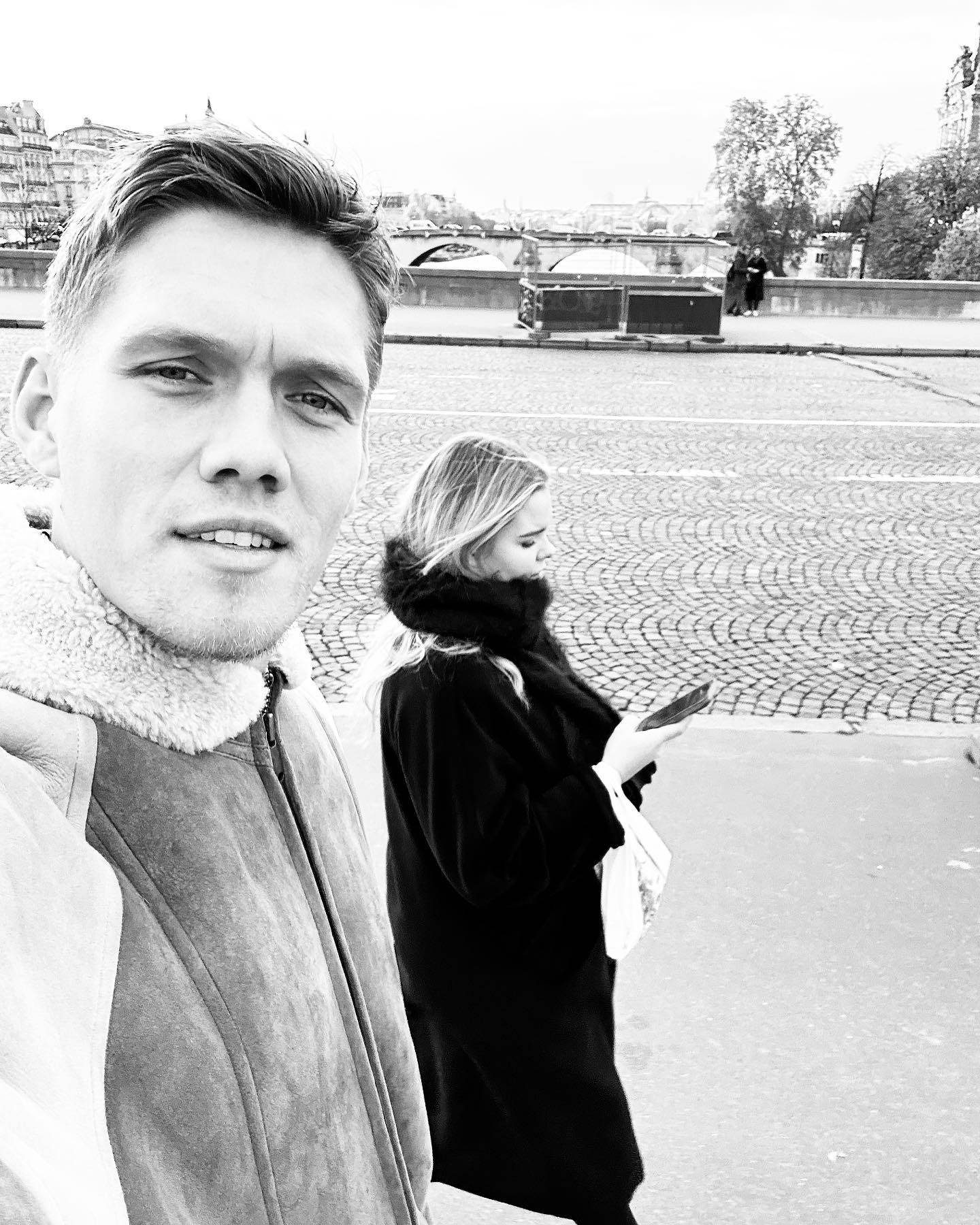 Jannik Vestergaard與妻子自拍 壁紙 — 一名男子在鵝卵石橋上自拍，而一名身穿深色外套的女子手持電話走過。