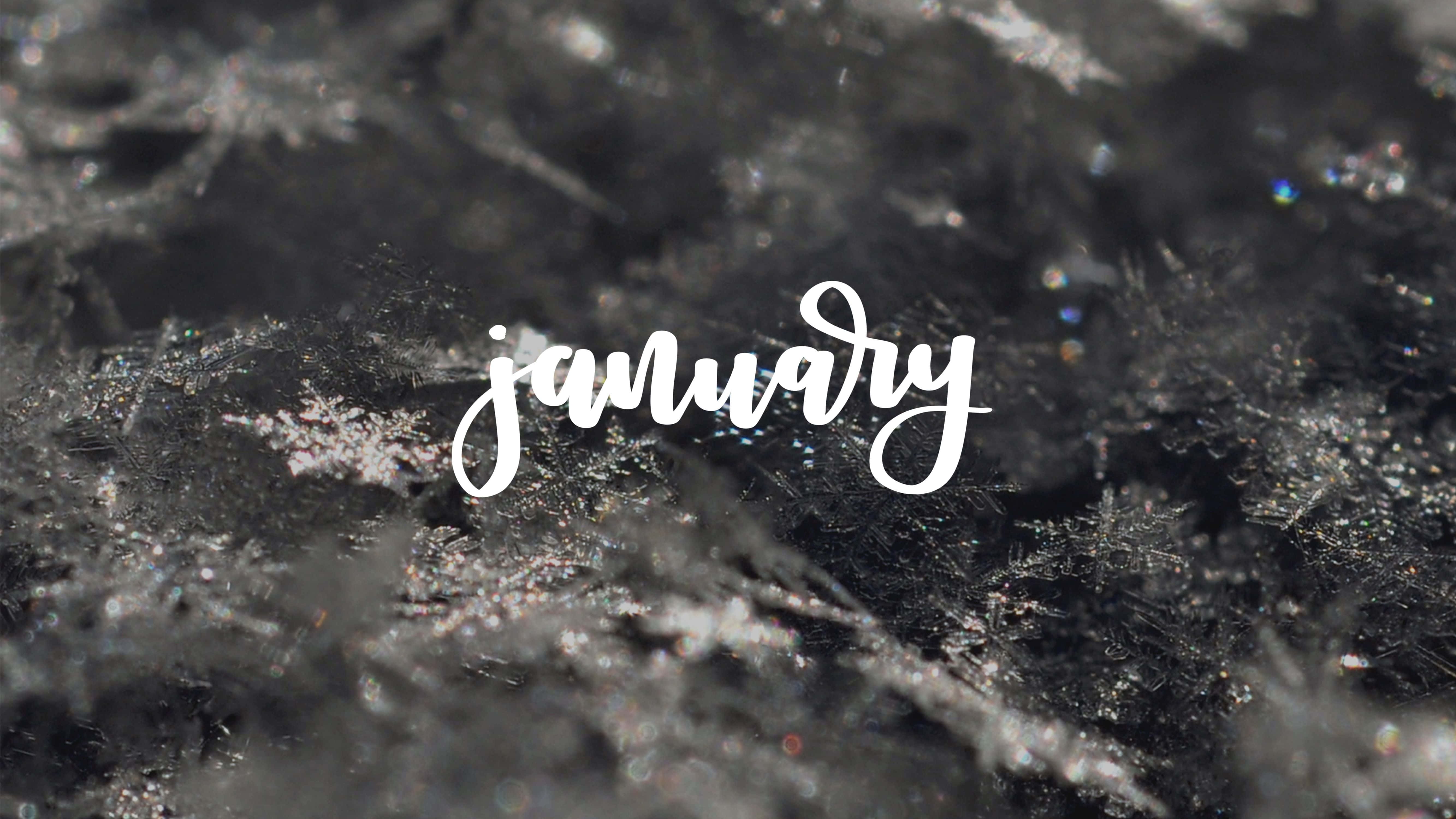 一月 桌布 壁紙 — 「january」這個詞以優雅的白色草書浮現在一個帶有閃爍霜狀細節的紋理深色表面上。