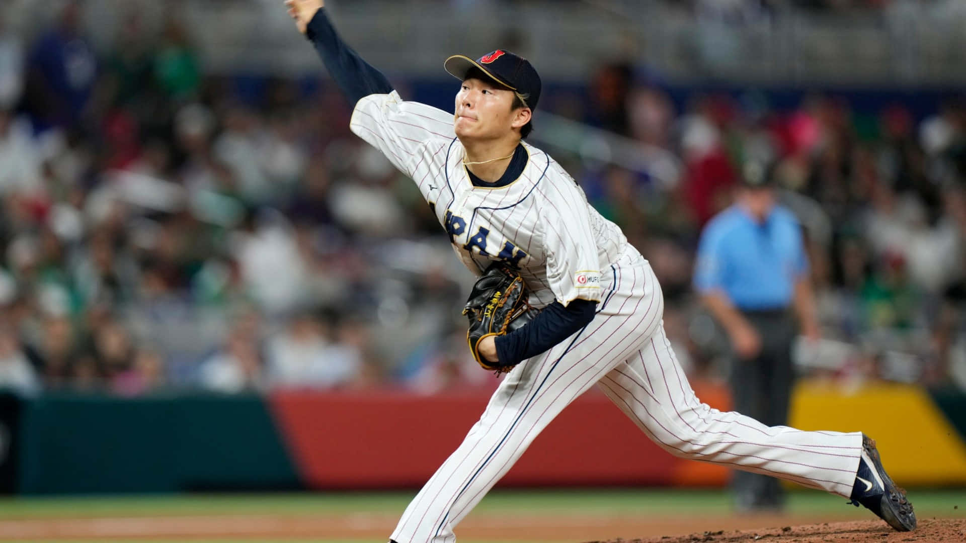  壁紙 — 一位身穿條紋球衣的日本棒球投手在球場燈光下投出強力一球，背景是模糊的人群。