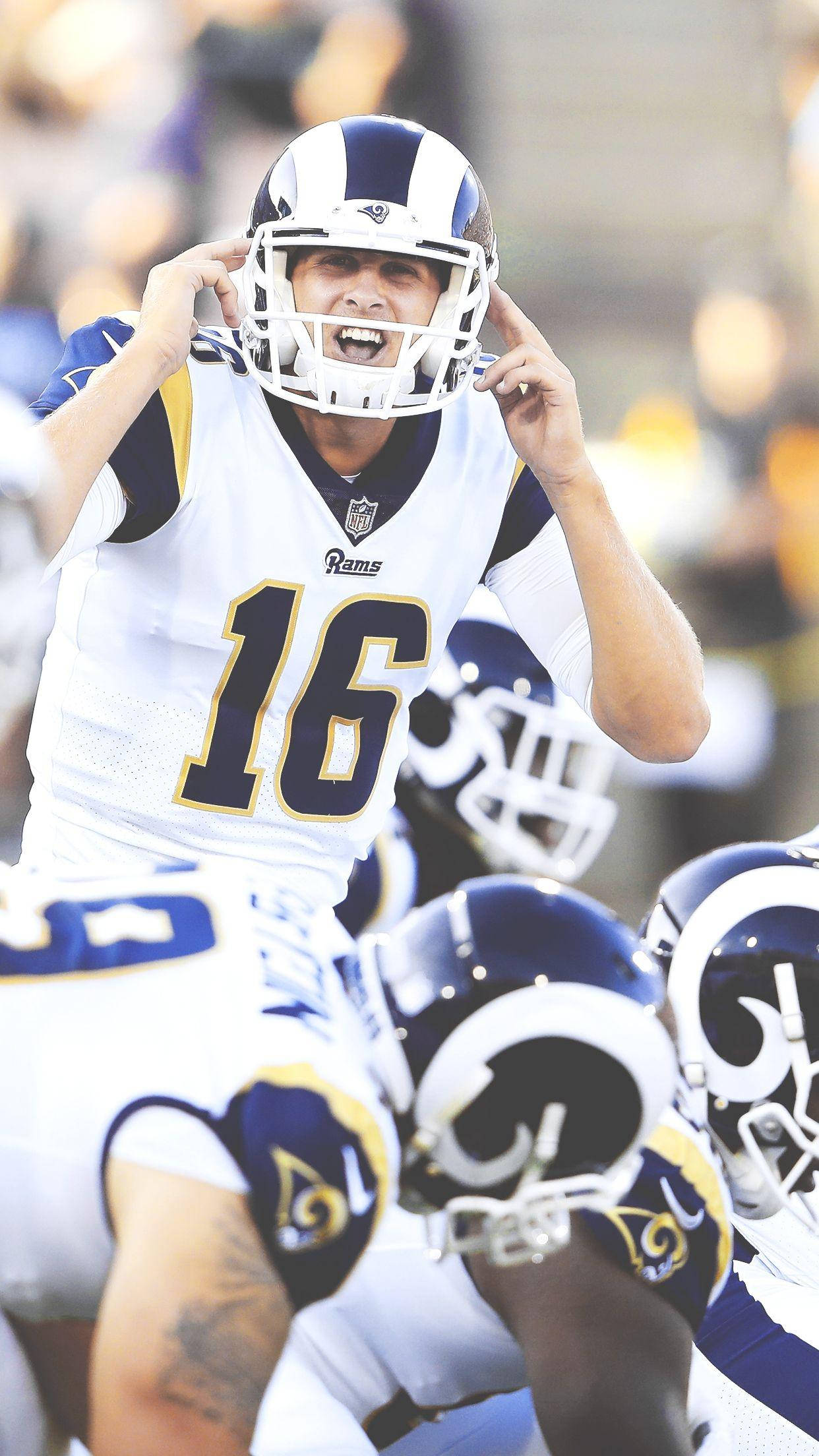 美國職業足球員賈瑞德·高夫（Jared Goff）效力洛杉磯公羊隊 壁紙 — 一名身穿白色和藍色球衣的洛杉磯公羊隊四分衛在美式足球比賽中專注地調整頭盔。