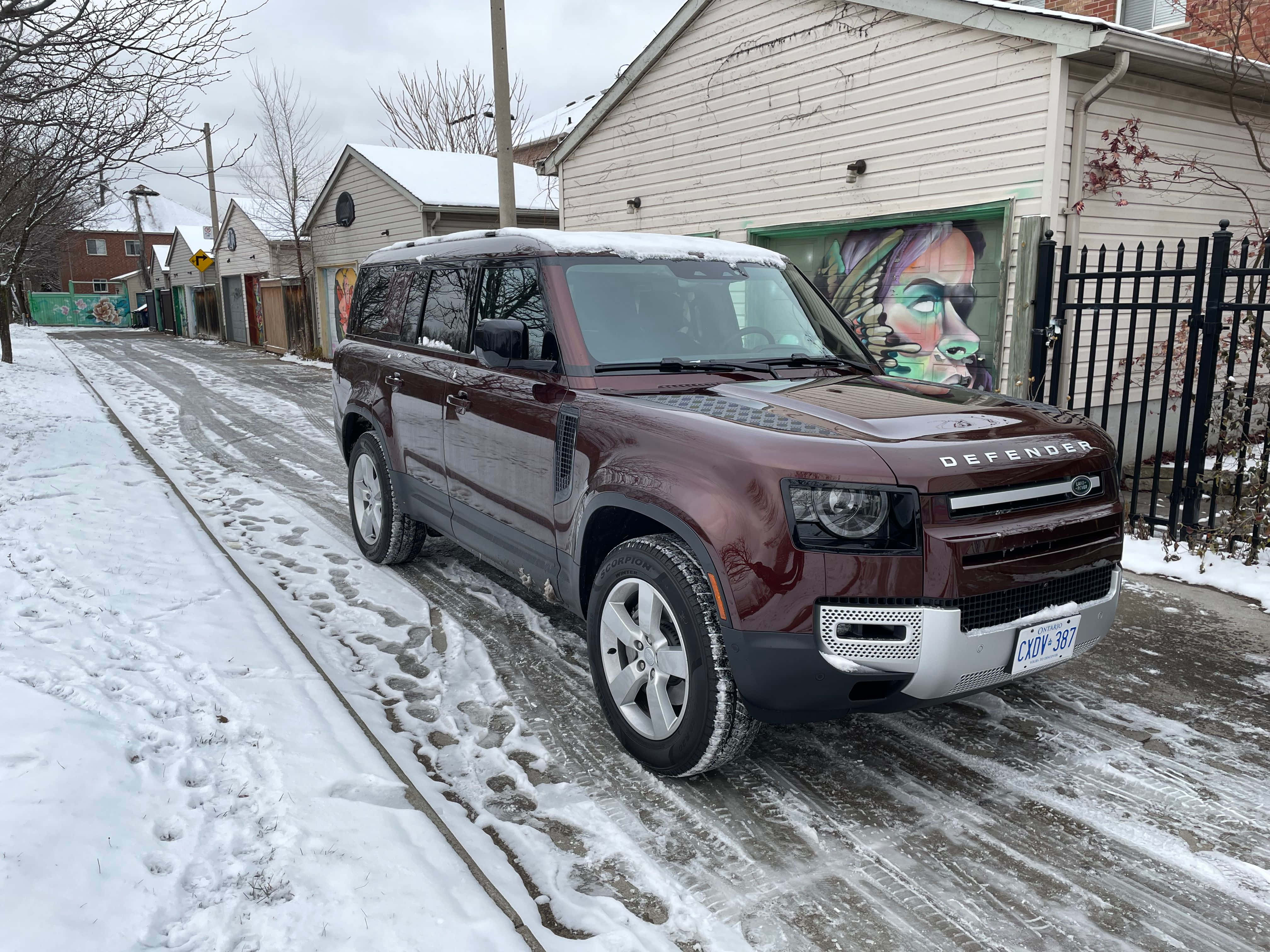 Land Rover Defender 桌布 壁紙 — 一輛酒紅色嘅Land Rover Defender停泊喺鋪滿雪嘅住宅街道旁邊，隔籬係一個佈滿塗鴉嘅車庫。