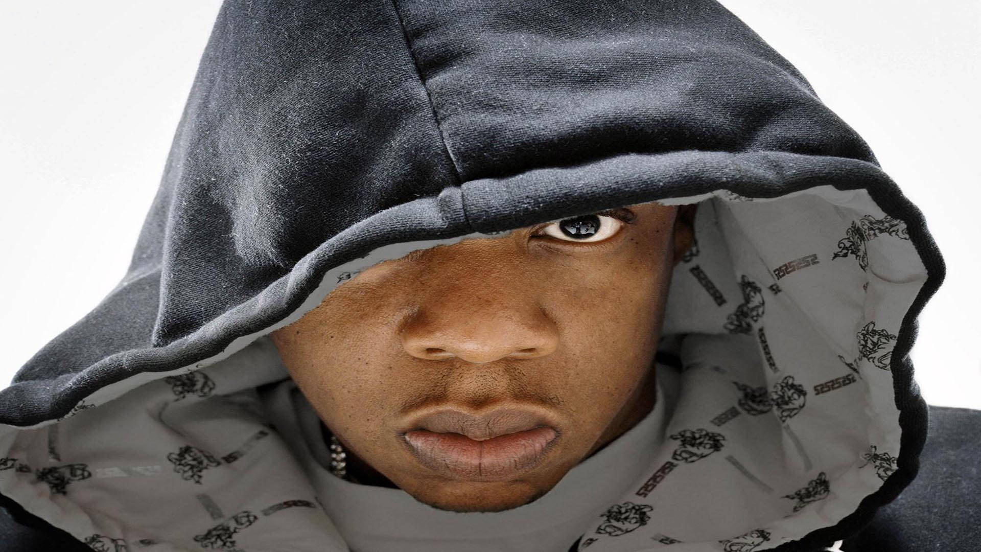 Jay-Z 戴連帽衫 壁紙 — 一個穿著深色連帽衫的人，在純白背景上露出一隻眼睛，凝視著。