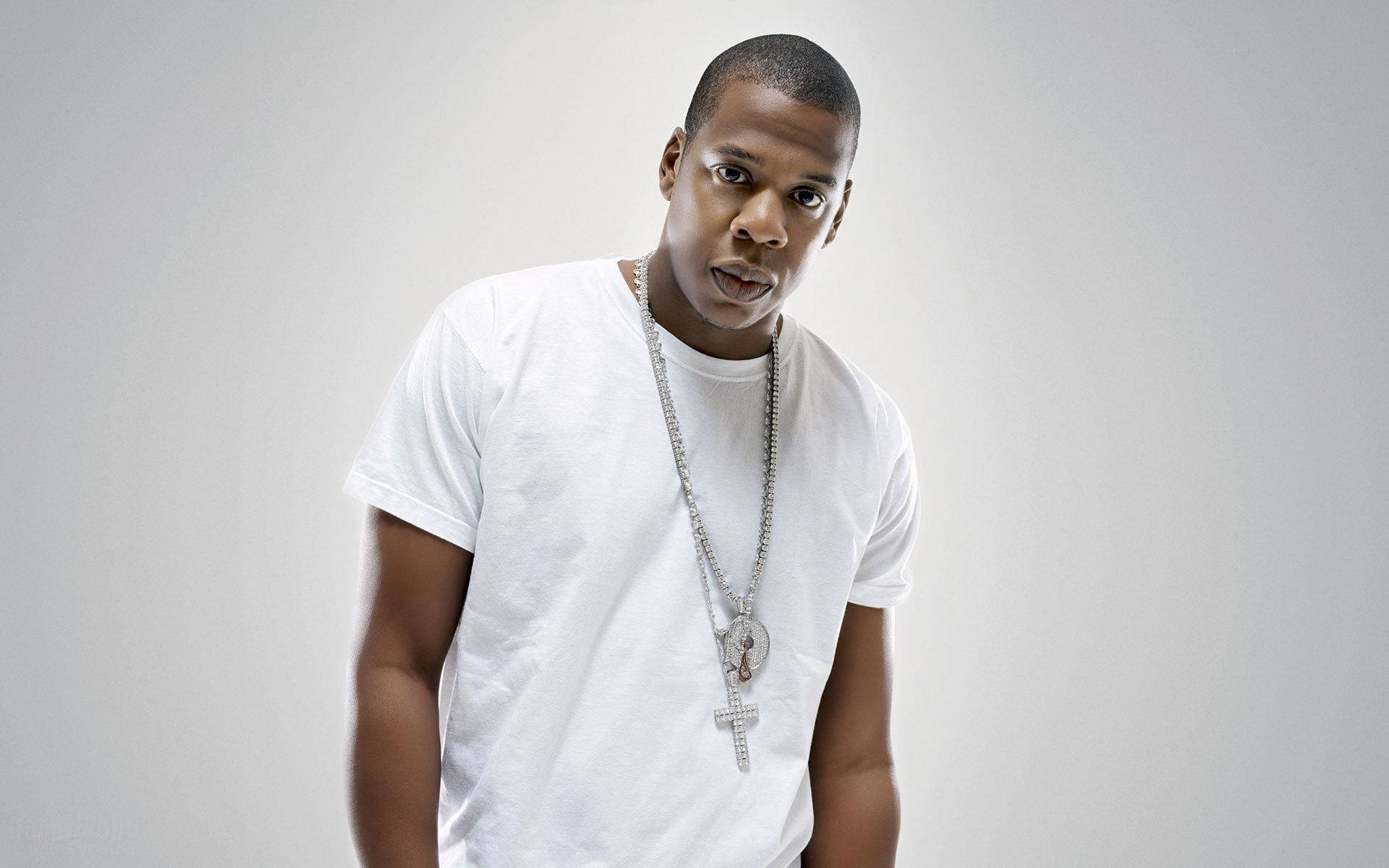 Jay-Z 攝影棚拍攝 壁紙 — 一名身穿白色T恤和銀色鏈條項鍊的男子，在純灰色背景前擺出驚訝的表情。