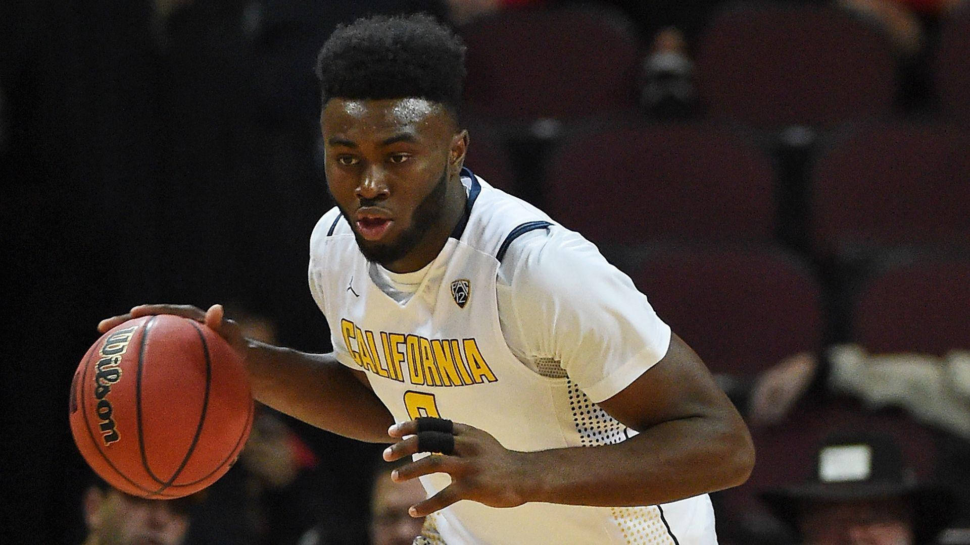 Jaylen Brown 加州大學時期 壁紙 — 一名專注的籃球運動員身穿白色加州球衣，在室內比賽中運著橙色Wilson籃球，背景是模糊的紅色座位。