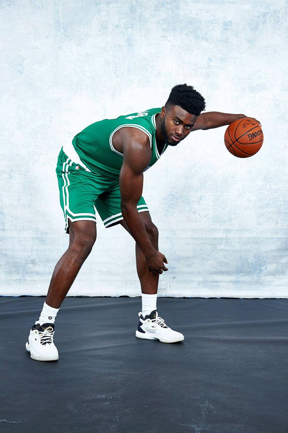 Jaylen Brown 波士頓媒體日 壁紙 — 一名身穿綠色球衣的籃球運動員，在帶有紋理的灰色背景下，專注而有力地運球。